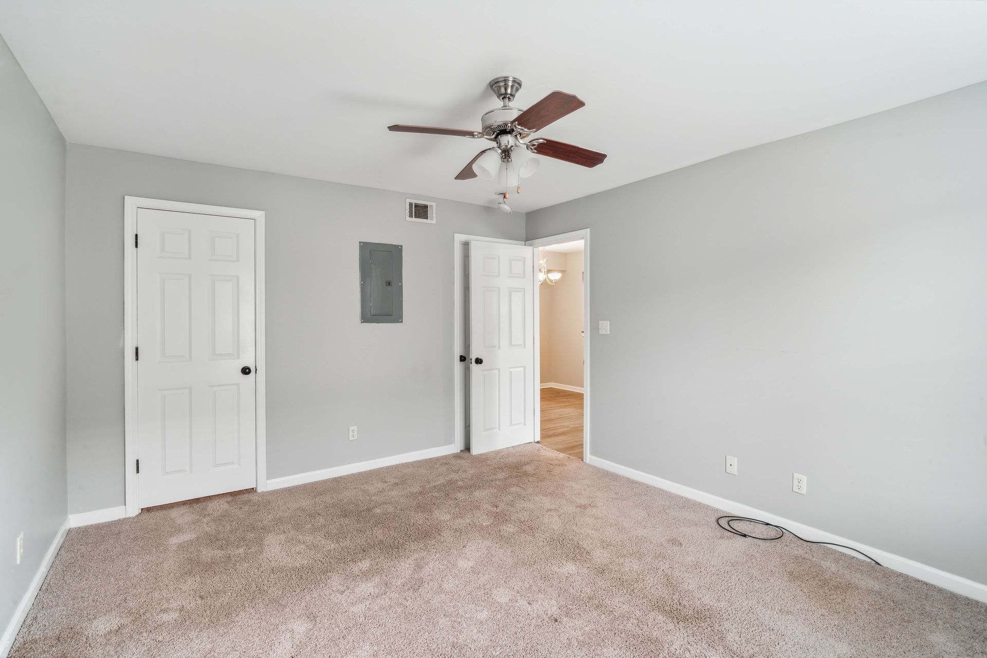 Empty carpeted bedroom with gray walls, white closet doors, ceiling fan, and open doorway to hallway