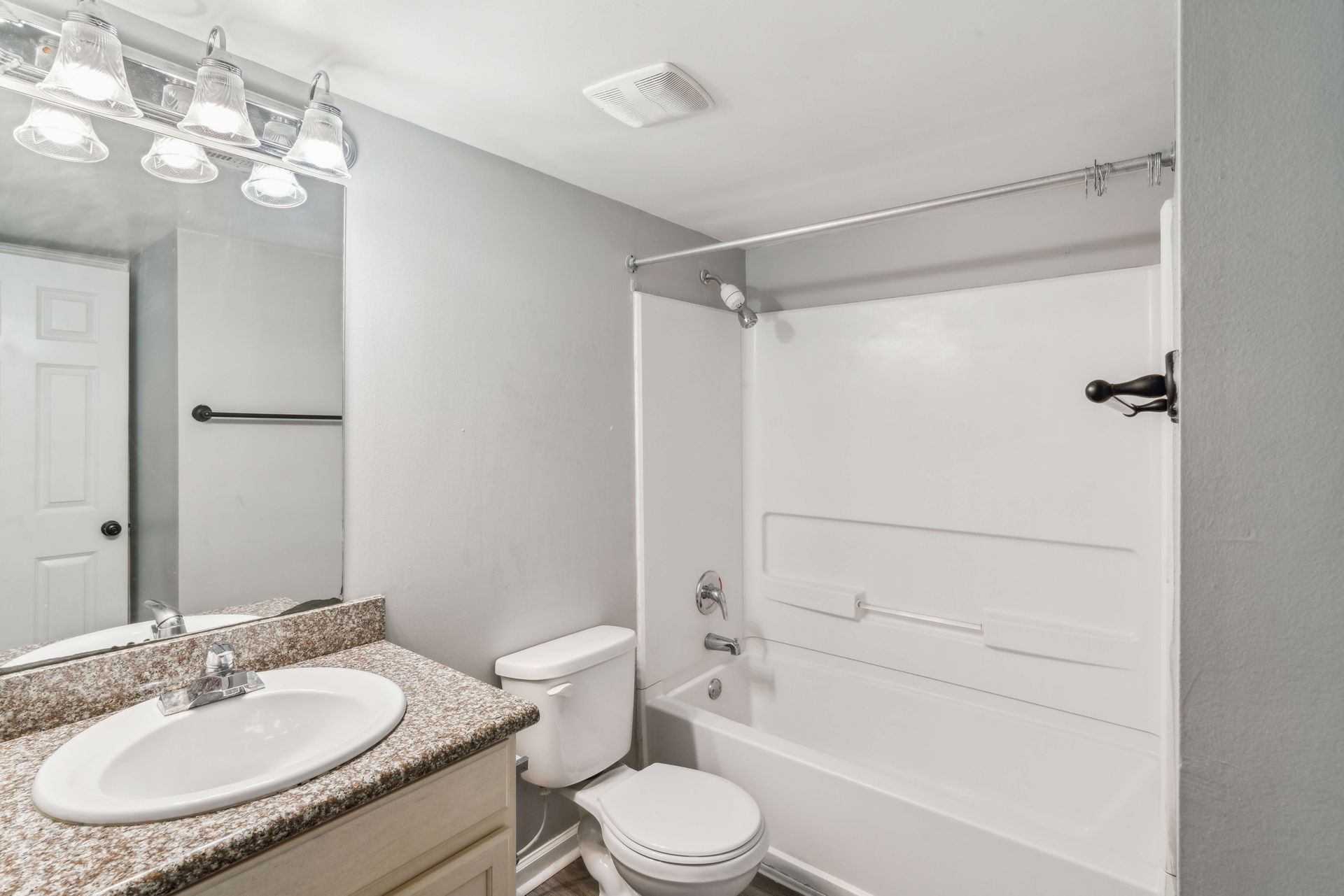 Small white bathroom with vanity sink, toilet, mirror, and bathtub with shower curtain rod.