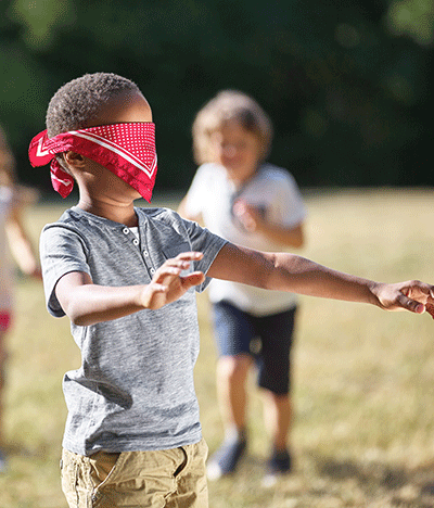 a blindfolded young afro-american boy playing in the park with other children