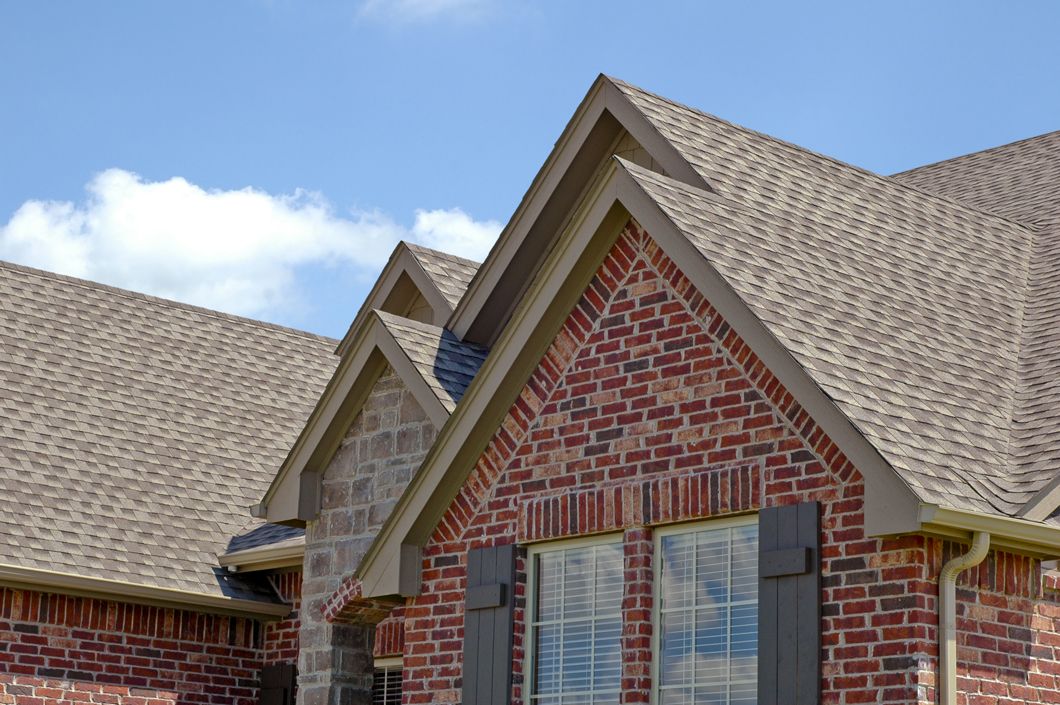 A brick house with a brown roof and black shutters.