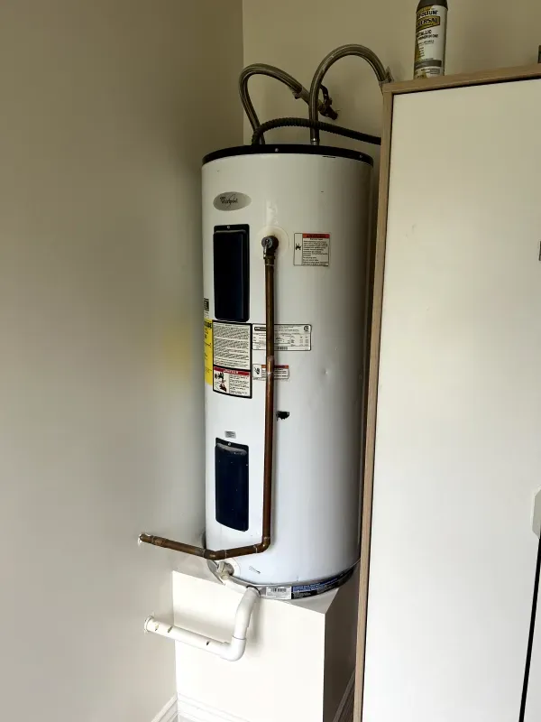 A white water heater is sitting in a corner of a room.