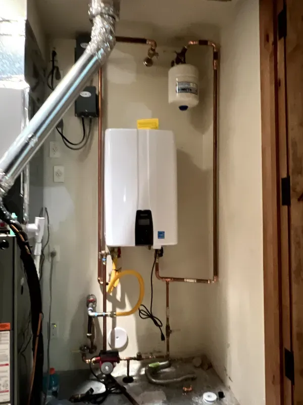 A white water heater is connected to a copper pipe in a room.