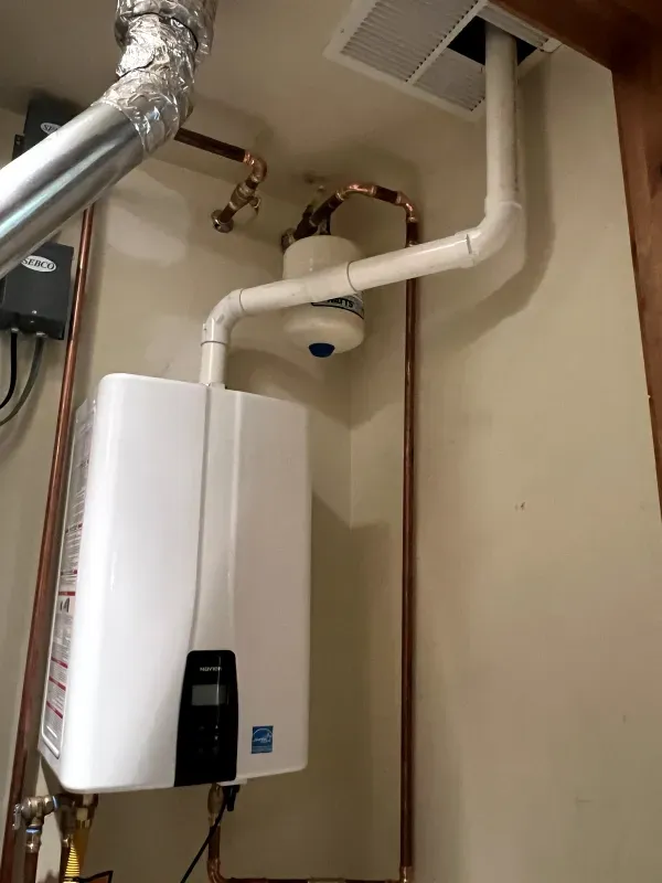 A white water heater is hanging from the ceiling in a room.