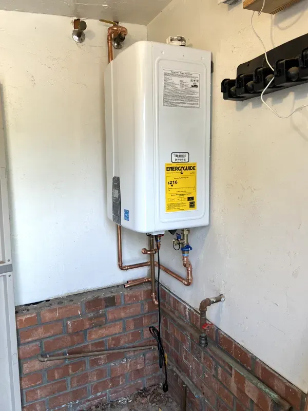 A white water heater is hanging on a brick wall in a room.
