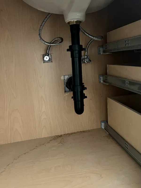 A sink with a black pipe underneath it in a cabinet.