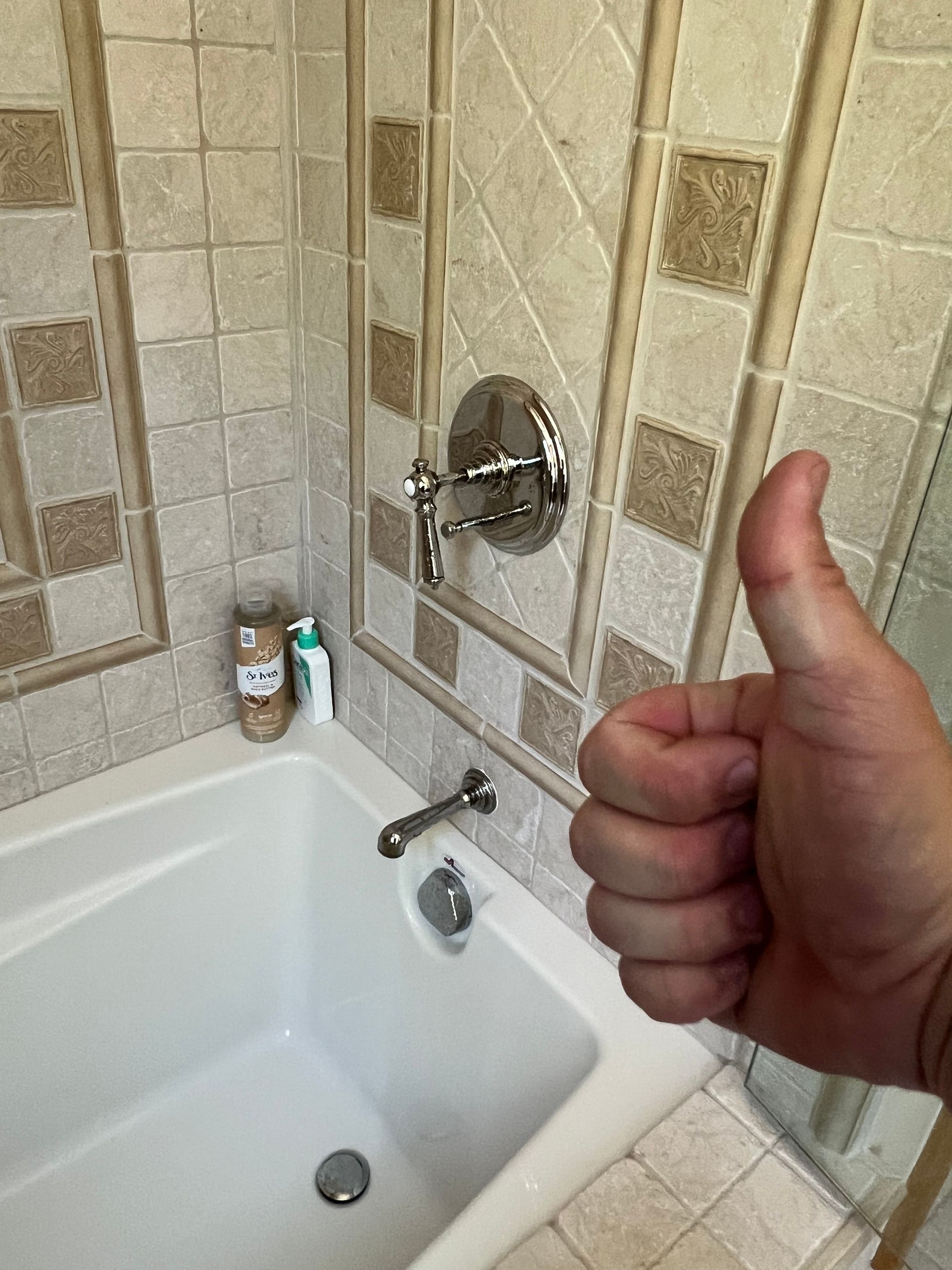 A person is giving a thumbs up in front of a bathtub.