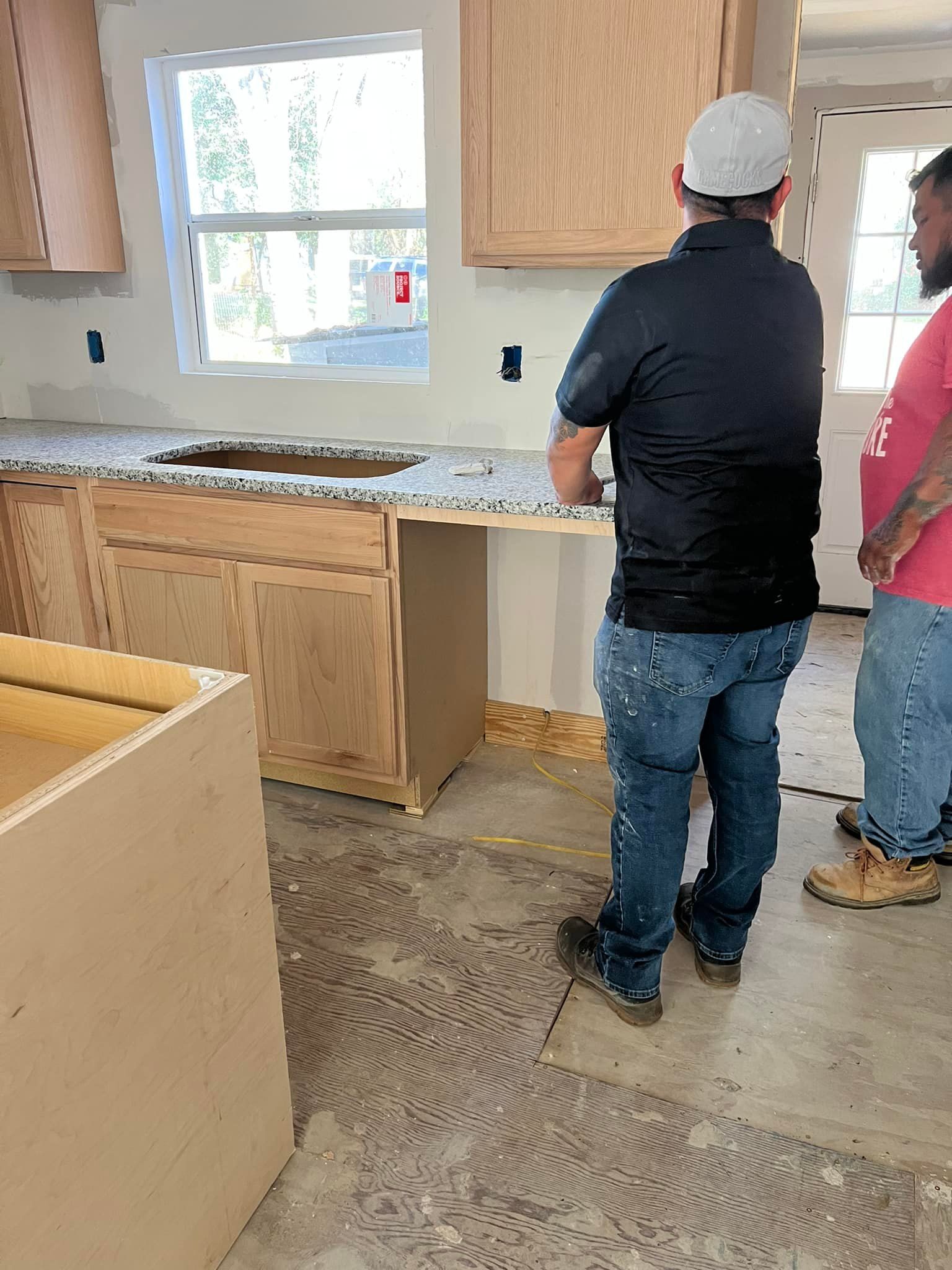 Two men in a kitchen under construction, examining countertop. Cabinets and sink in place.