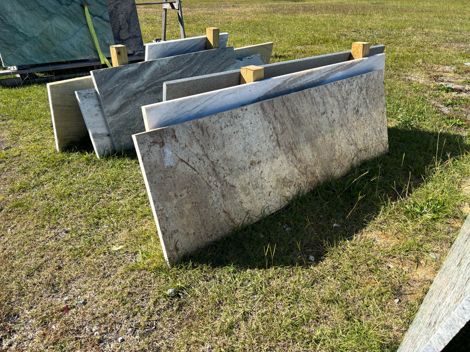 Slabs of granite leaning against wooden supports on grass. The slabs are various colors and textures.