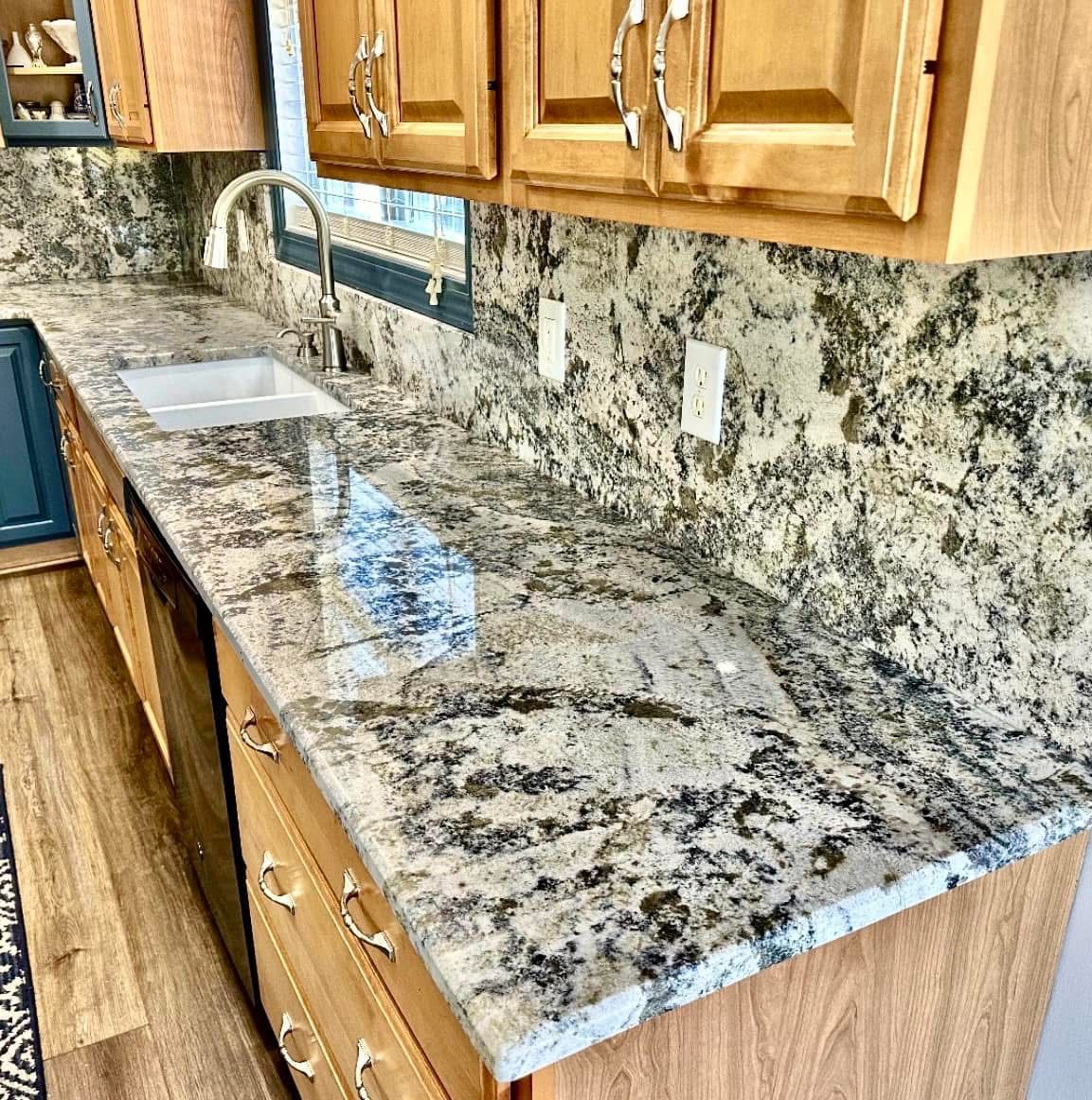 Kitchen countertop with light wood cabinets, granite, and stainless steel faucet and sink.