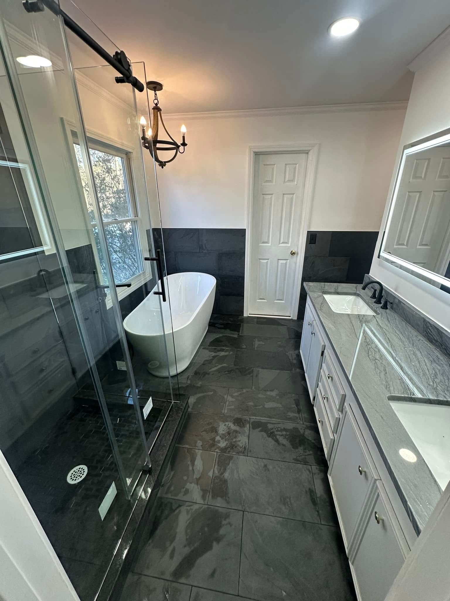 Modern bathroom with a freestanding tub, glass shower, and double vanity. Dark gray tile.