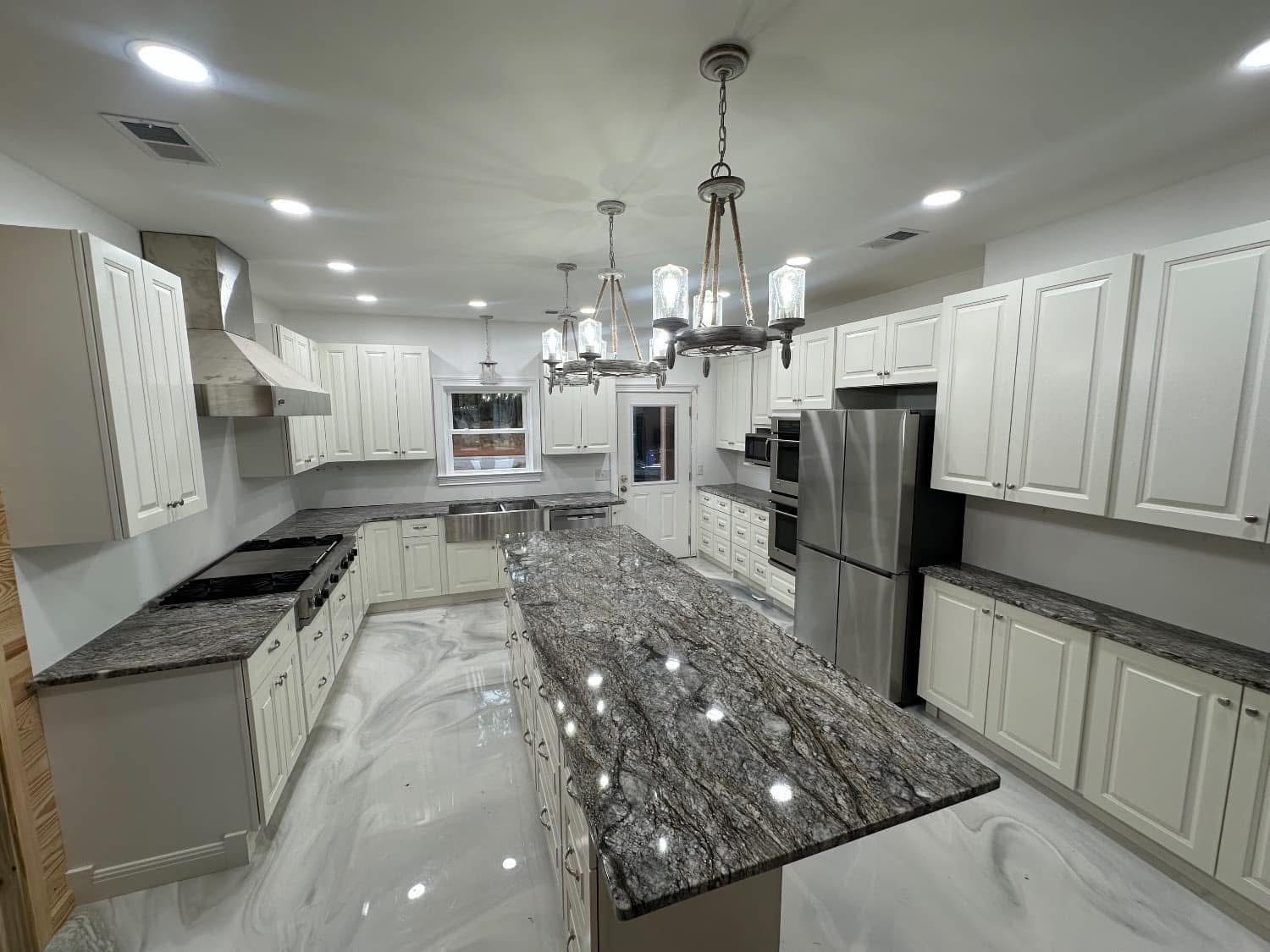 Bright white kitchen with a large island, granite countertops, and stainless steel appliances.