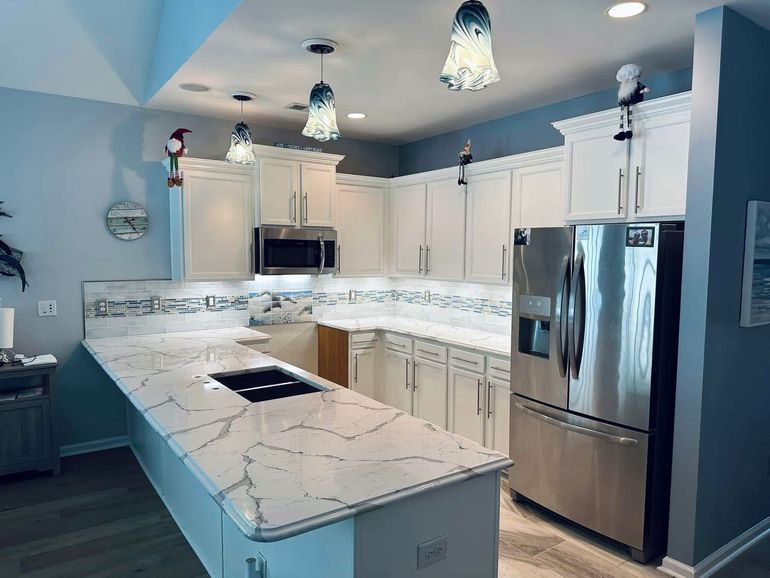 White kitchen with island, quartz countertops, stainless steel appliances, blue walls, and pendant lights.
