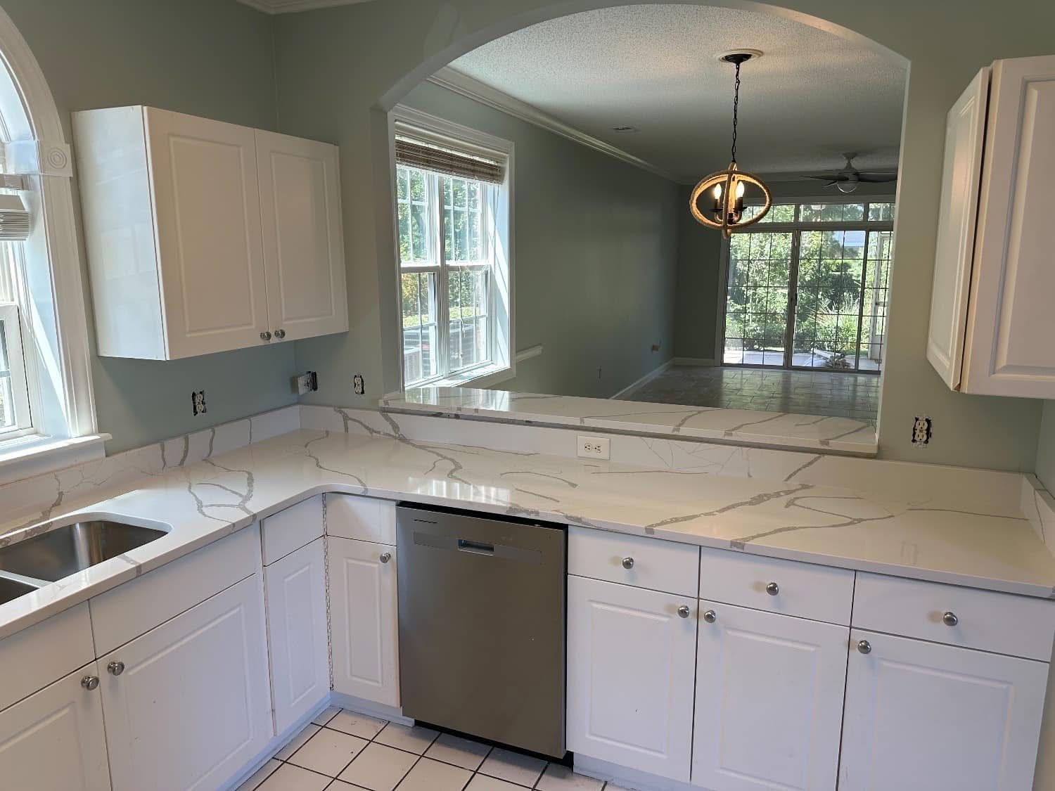 White kitchen with quartz countertops and a stainless steel dishwasher, opening into a room with a view.