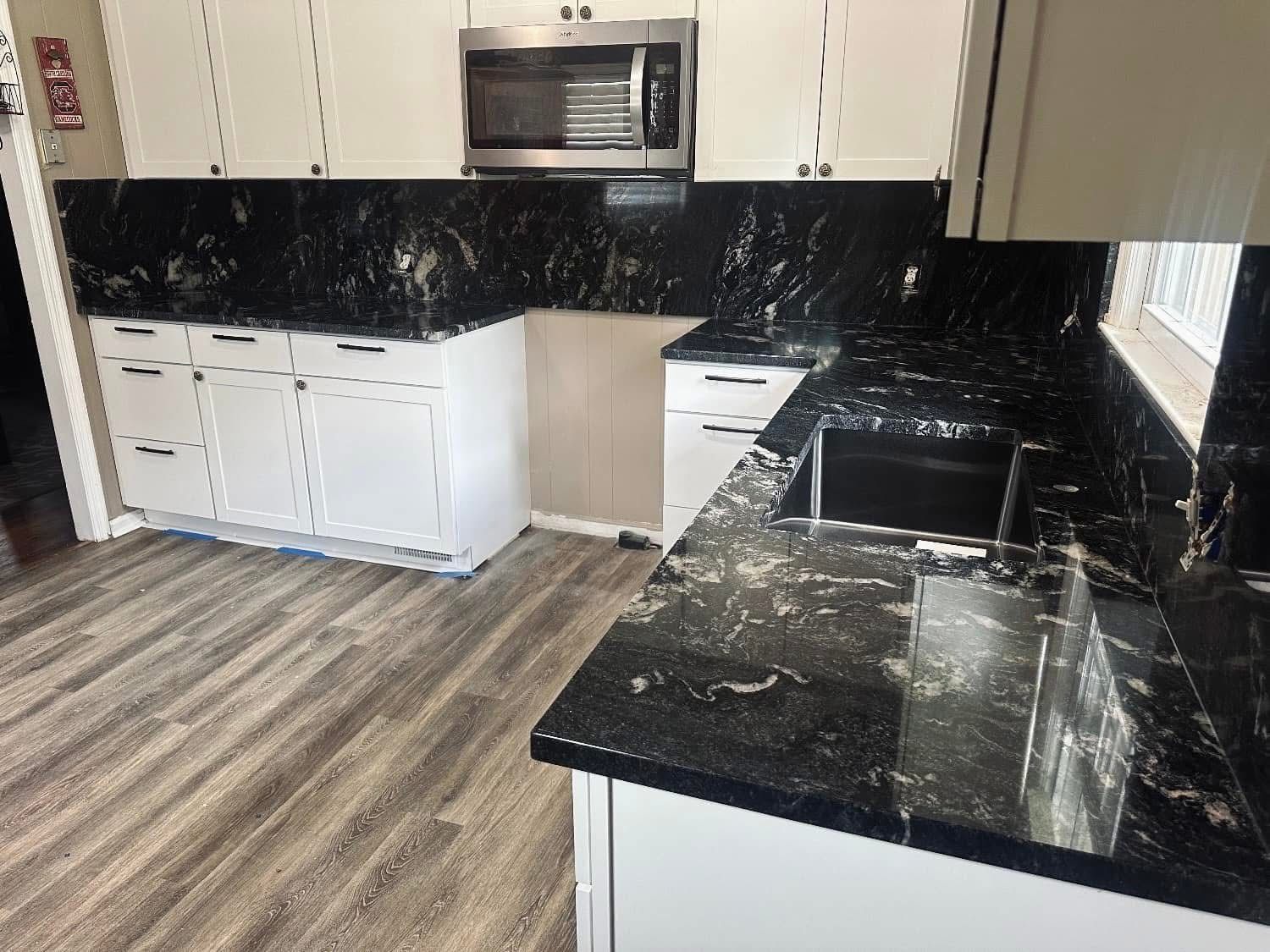 Kitchen with white cabinets, black granite countertops, and wood-look flooring.