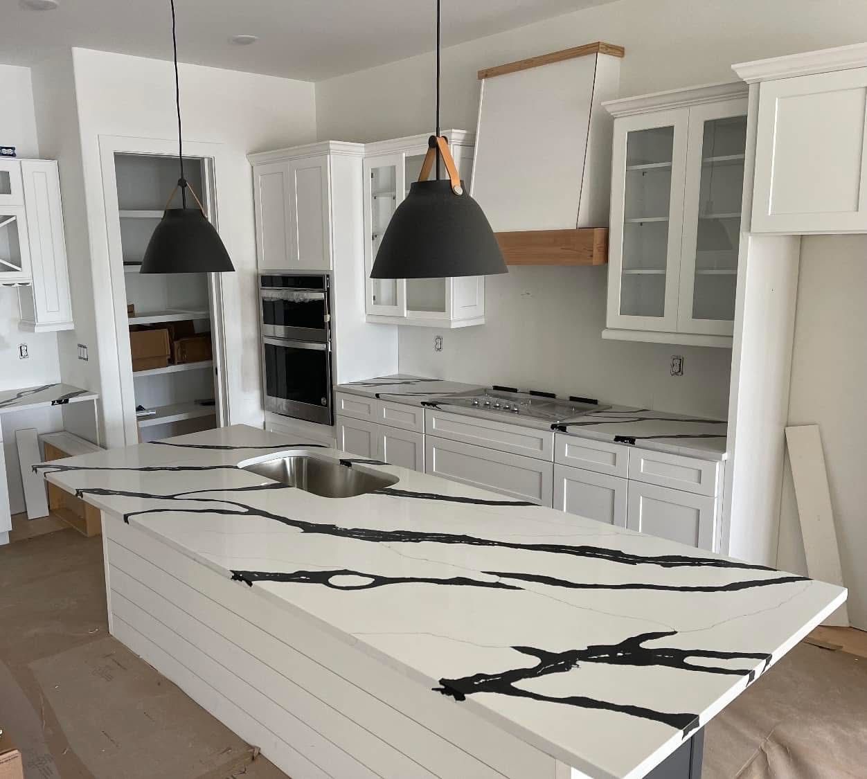 Kitchen with white cabinets, island with black veined countertop, two pendant lights, and unfinished elements.