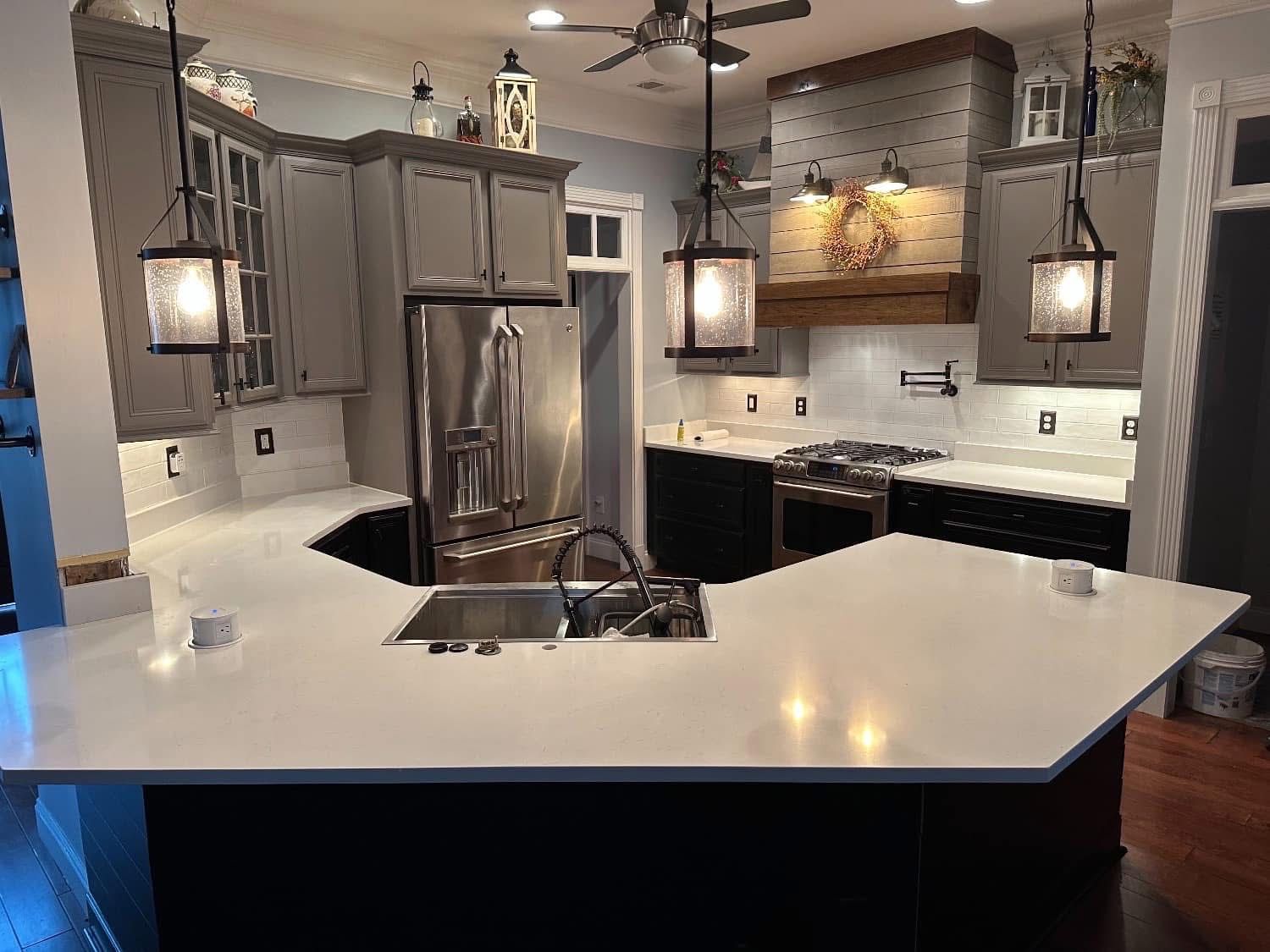 Modern kitchen with gray cabinets, white countertops, stainless steel appliances, and hanging lights.
