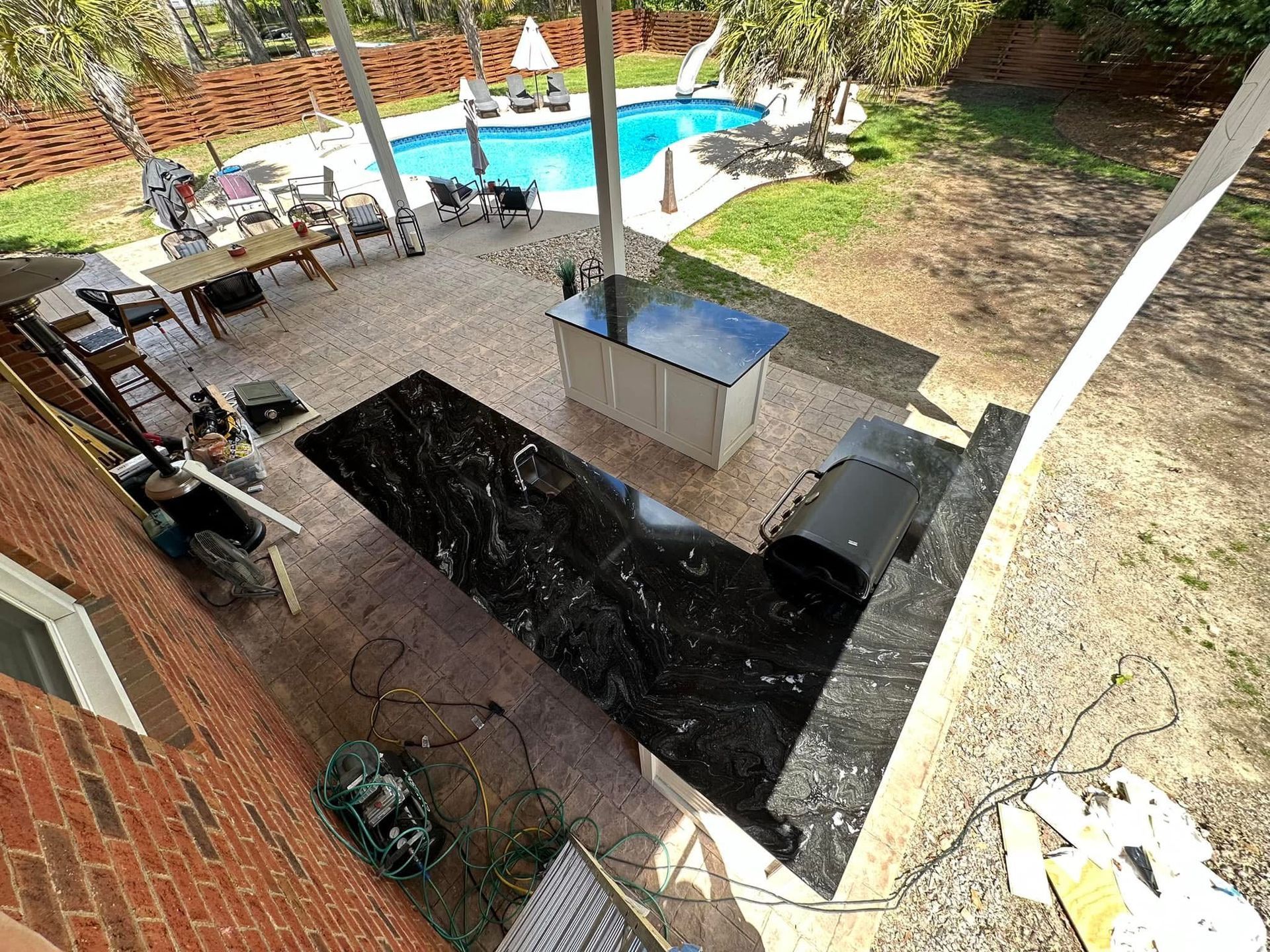 Backyard patio with granite countertop, grill, pool, and seating.