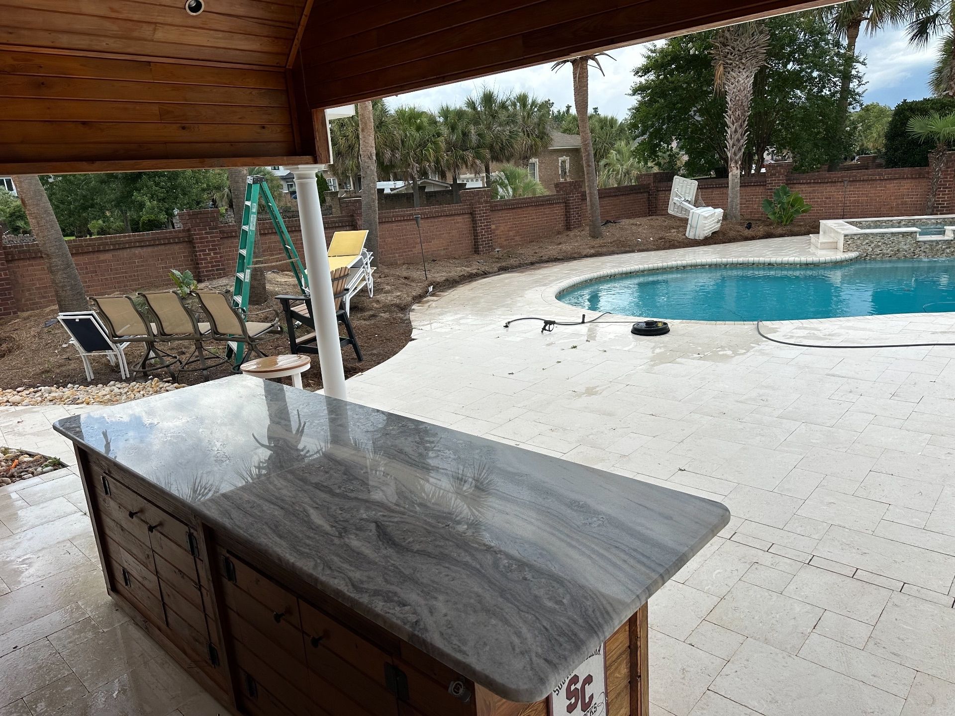 Outdoor bar with granite countertop overlooking a pool, patio, and brick wall.