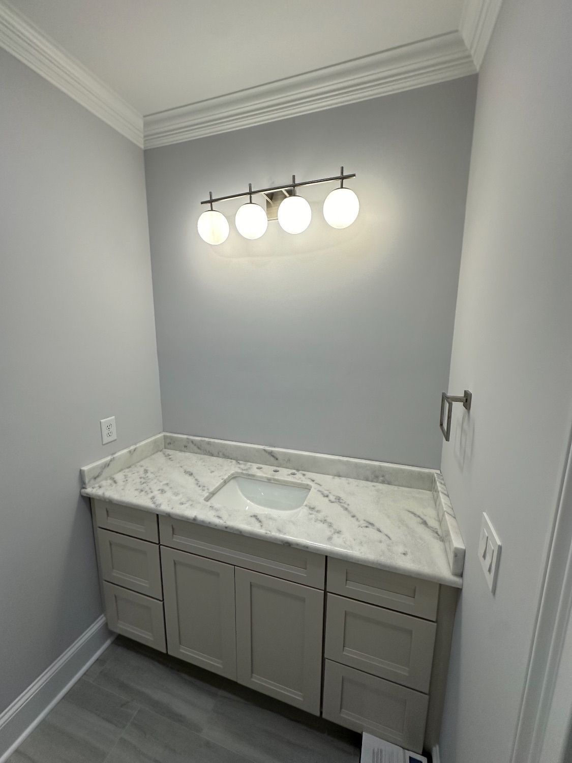 Bathroom with gray walls, white cabinets, marble countertop, and a four-light fixture.