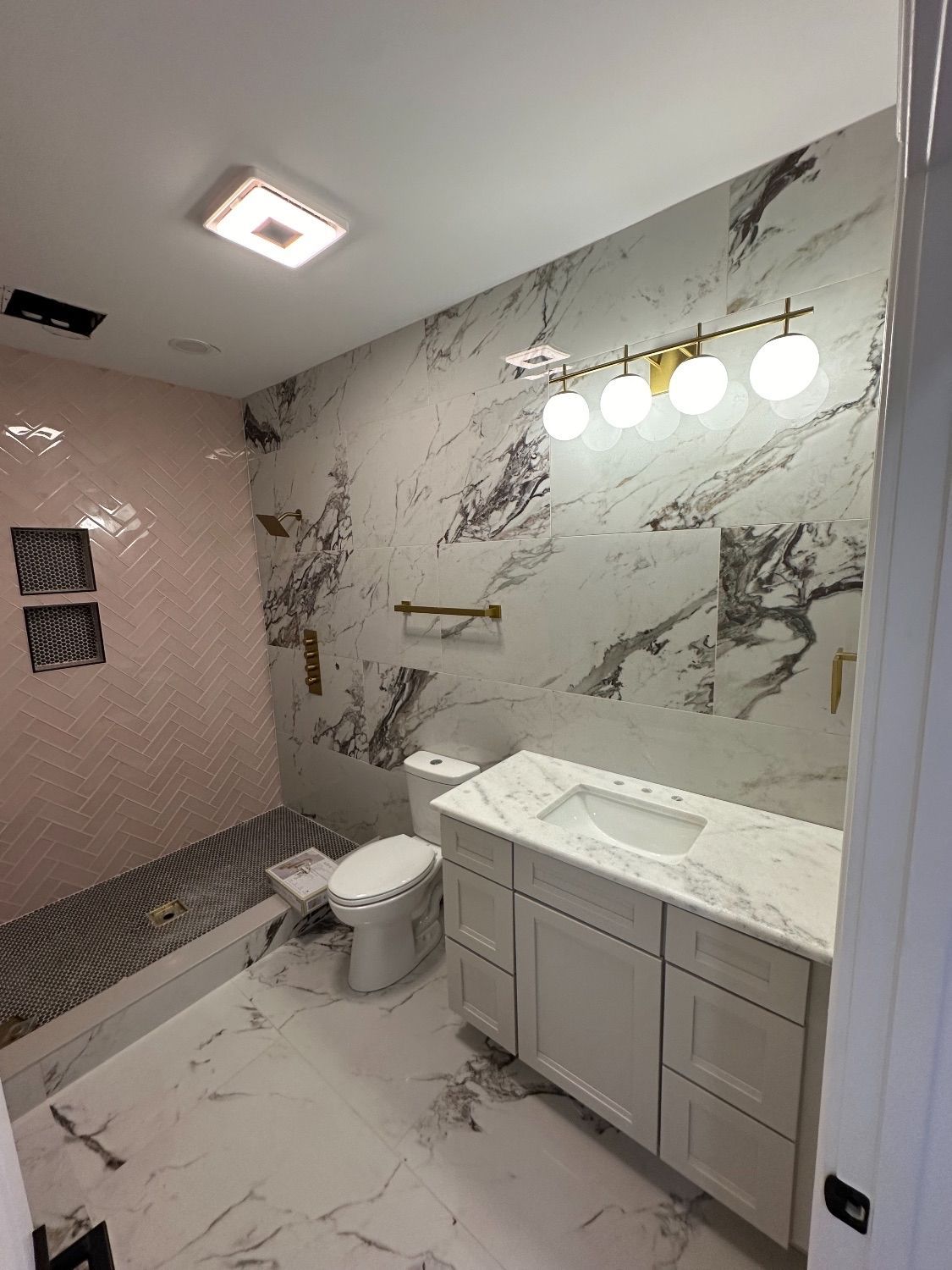 Modern bathroom with white marble tile and pink shower. White vanity, toilet, gold accents.