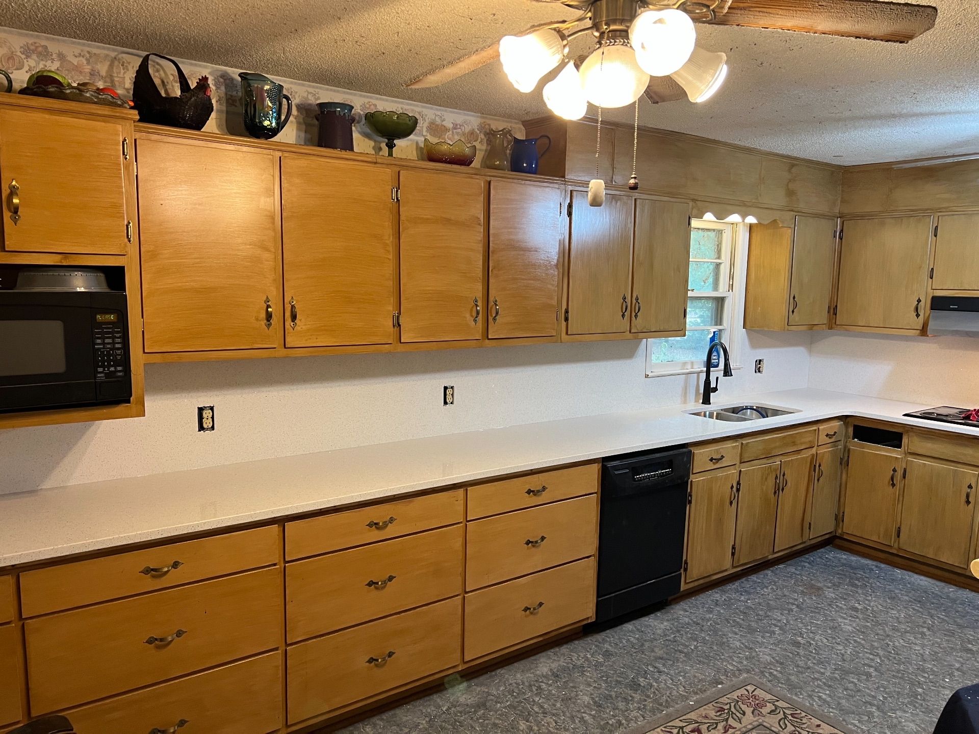 Kitchen with light wood cabinets, white countertops, black appliances, and a ceiling fan.