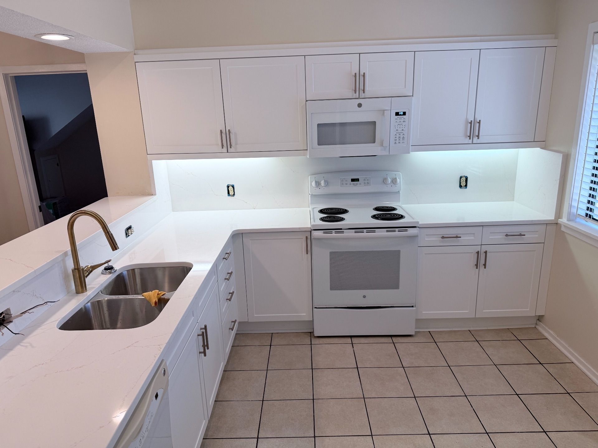 White kitchen with cabinets, countertops, and appliances. Includes a stove, microwave, and sink with a gold faucet.
