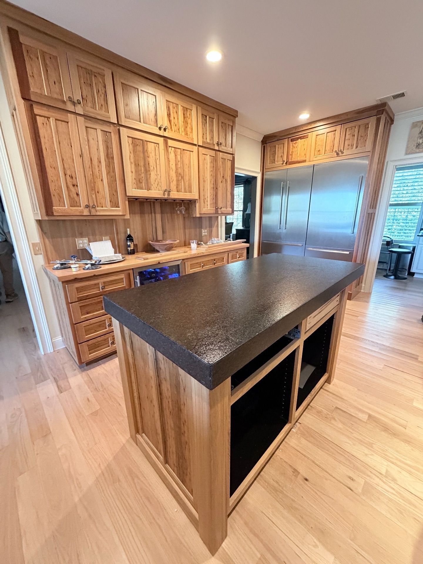 Kitchen with wooden cabinets and island, granite countertop, stainless steel refrigerator, and hardwood floors.