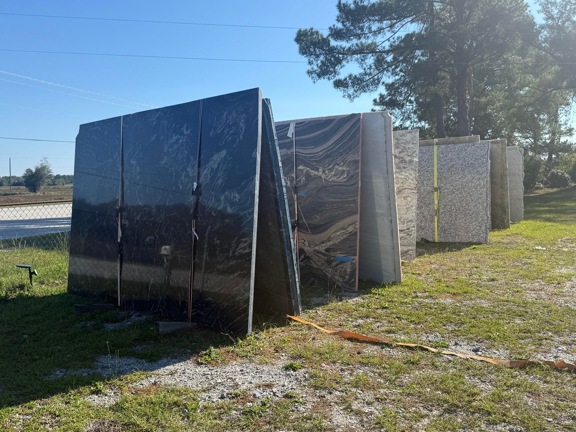 Granite slabs standing outdoors in a row, wrapped in plastic. Sunny day.