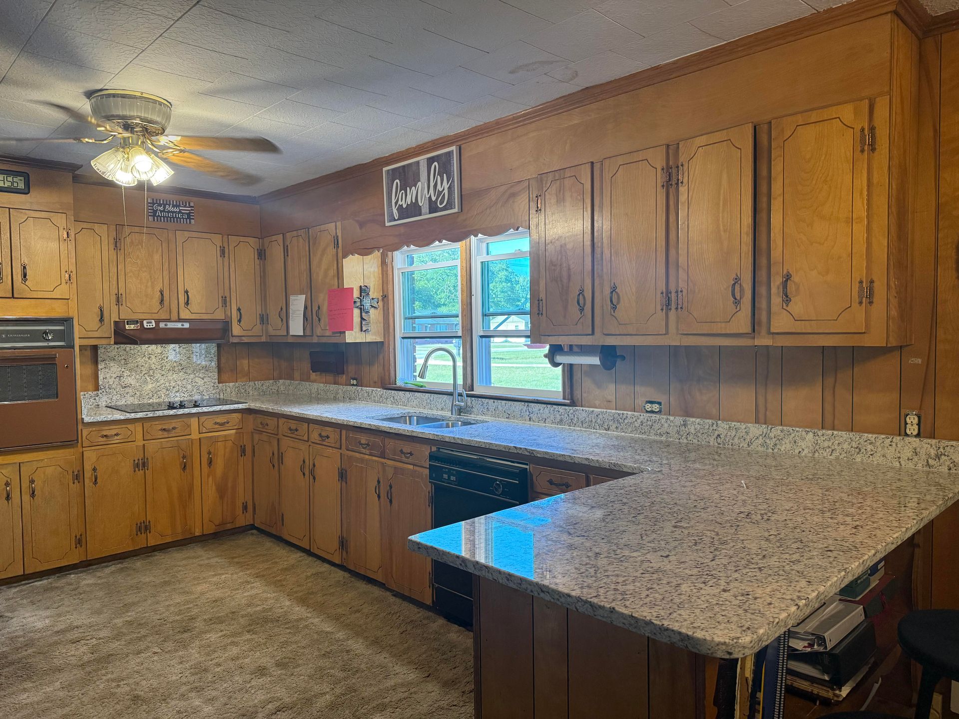 U-shaped kitchen with wood cabinets, speckled countertops, and a window above the sink.