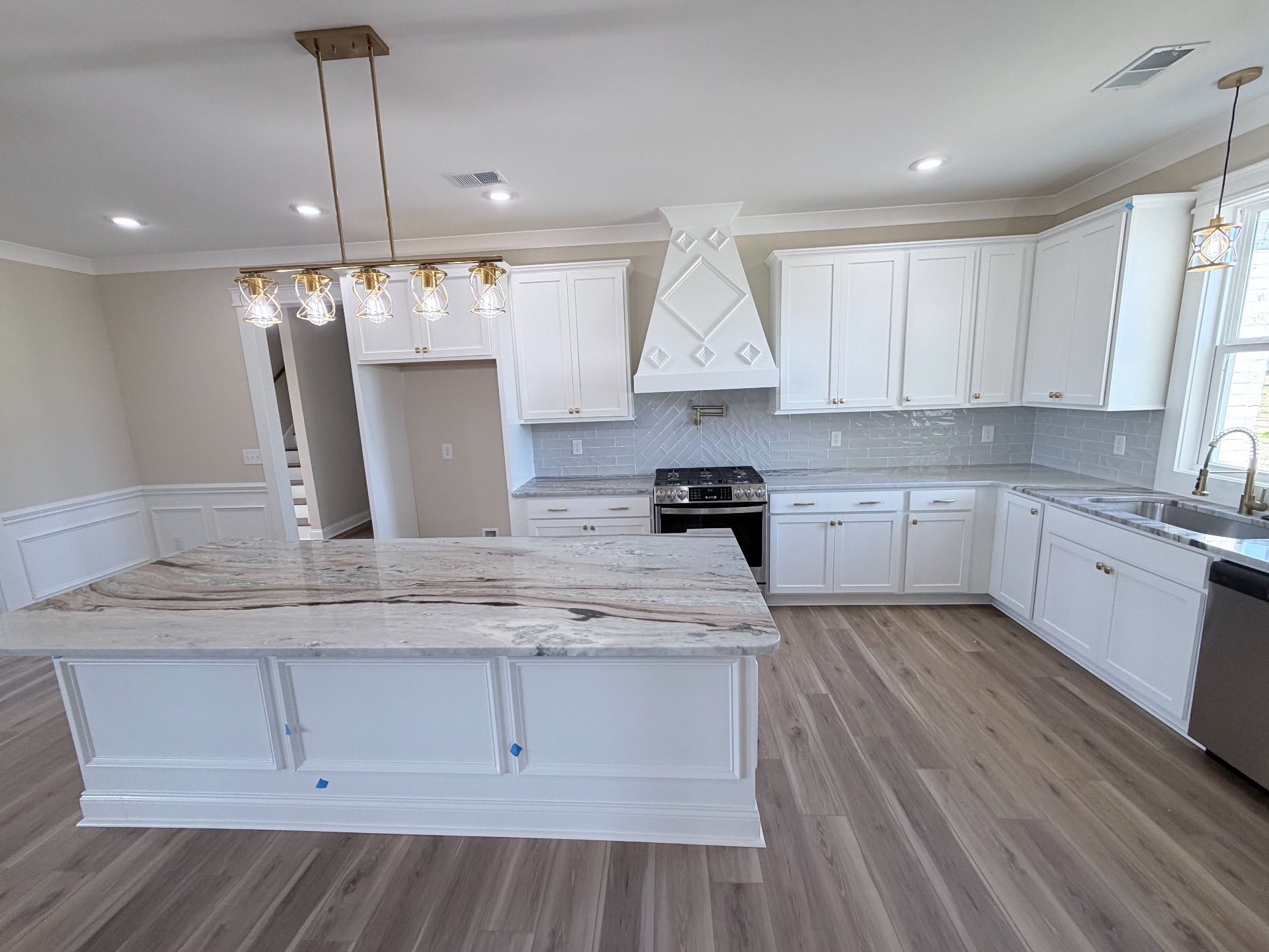 White kitchen with a large island, cabinets, and a range with a decorative hood.
