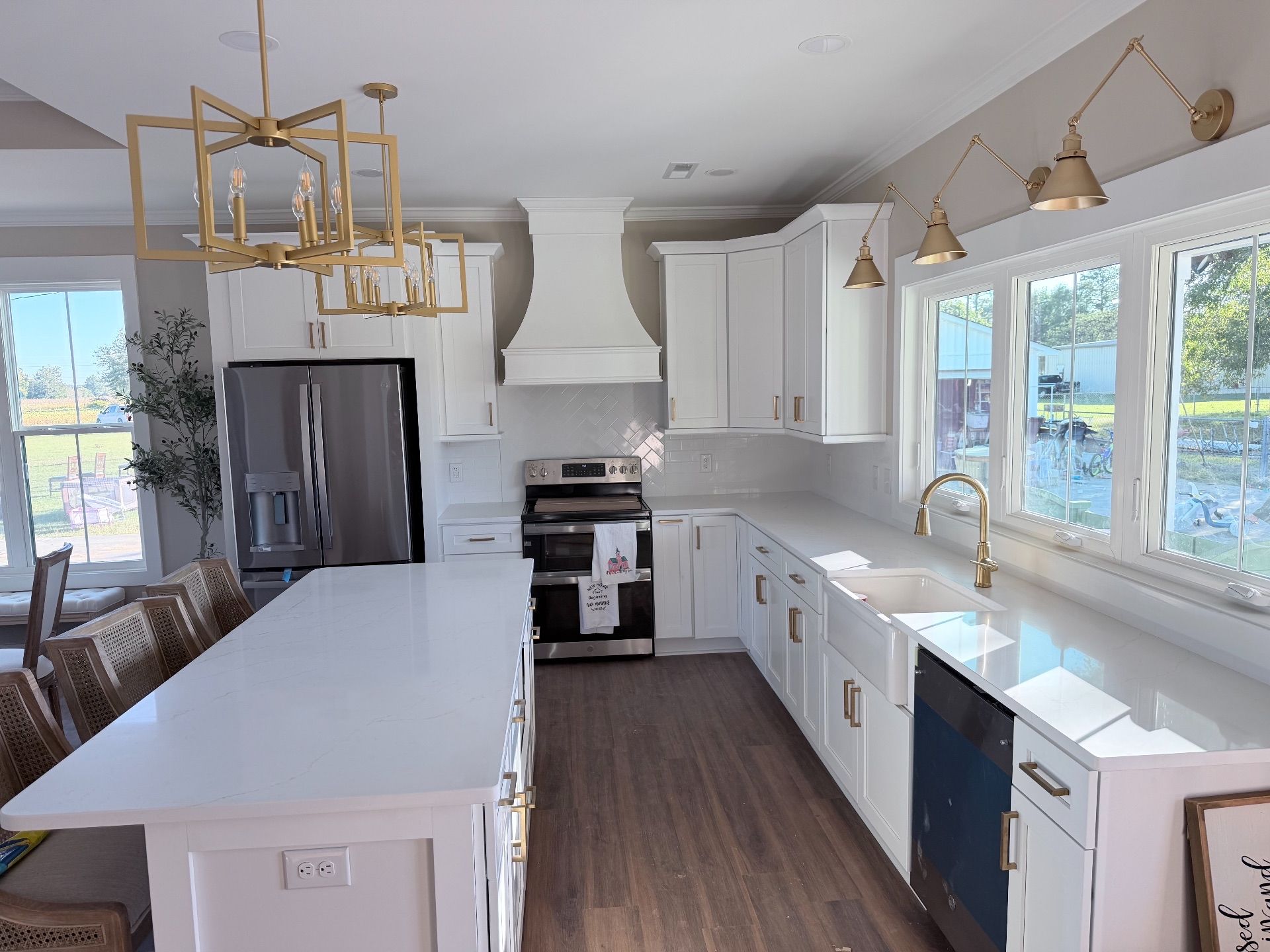 White kitchen with large island, stainless steel refrigerator, gold light fixtures, and white cabinets.