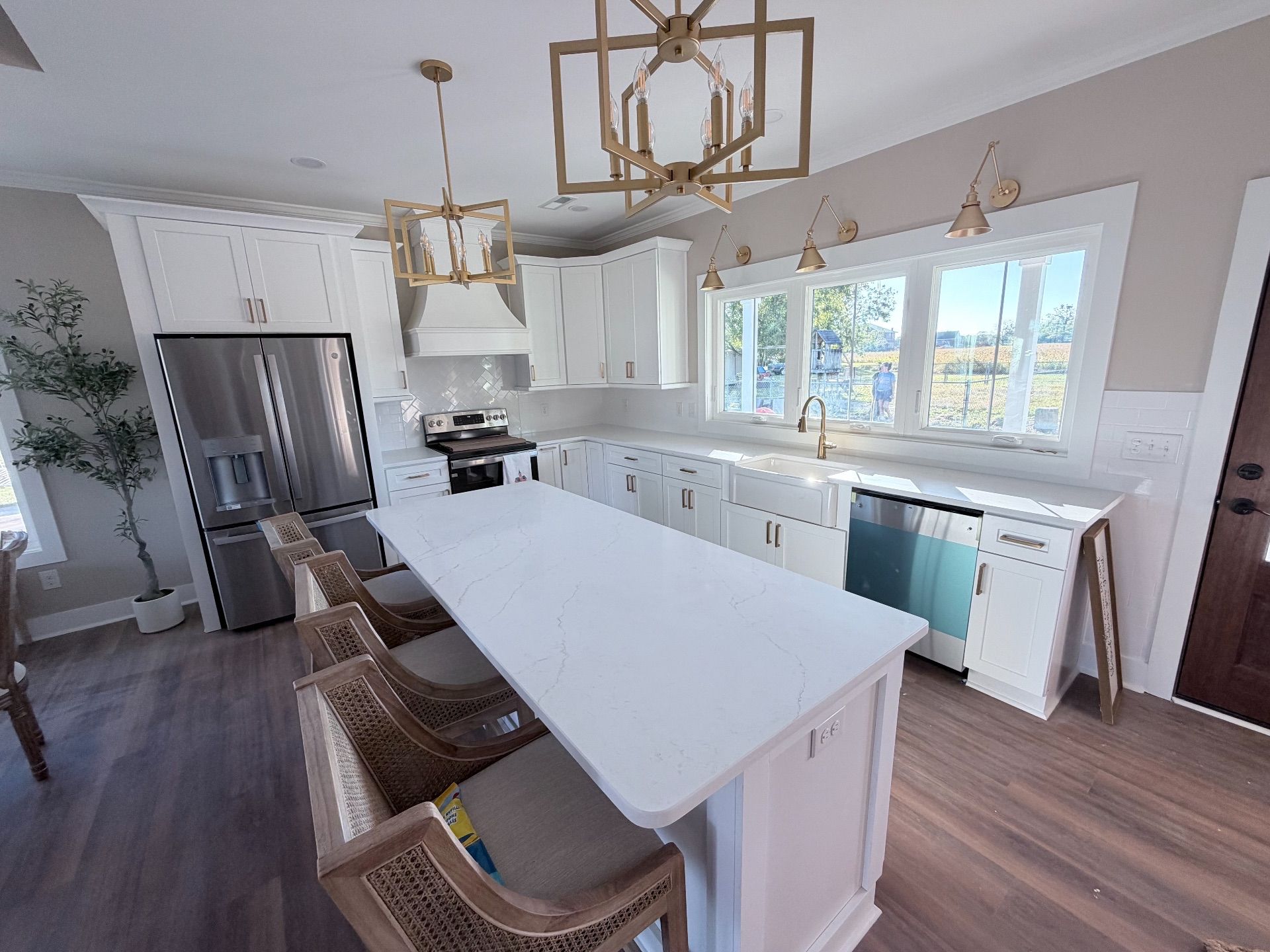 White kitchen with island, cabinets, stainless steel refrigerator, and wooden floors.