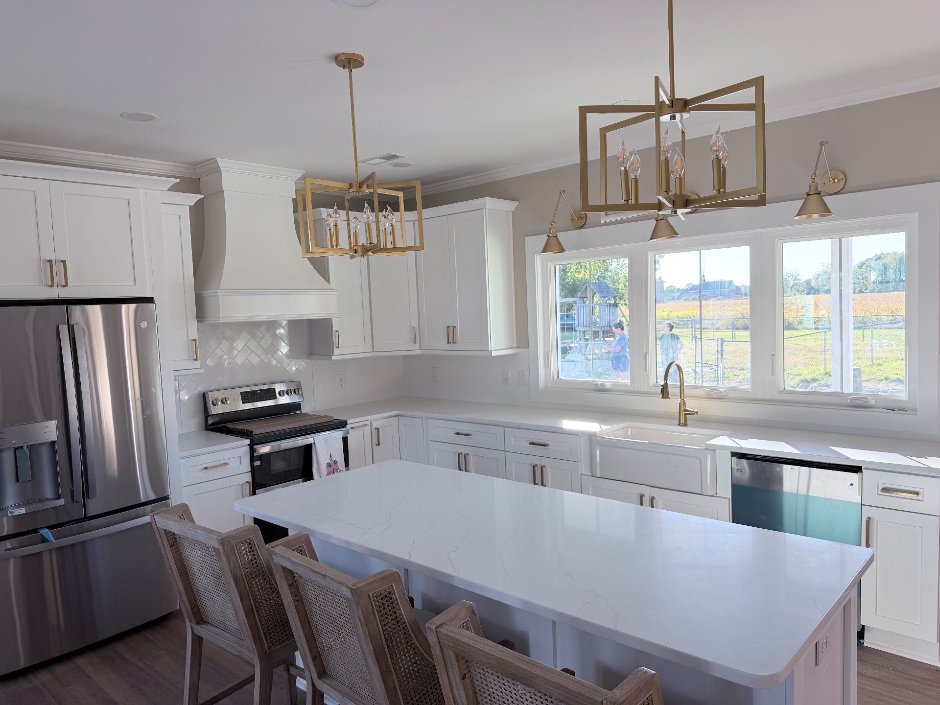 White kitchen with island, stainless steel appliances, and gold light fixtures.