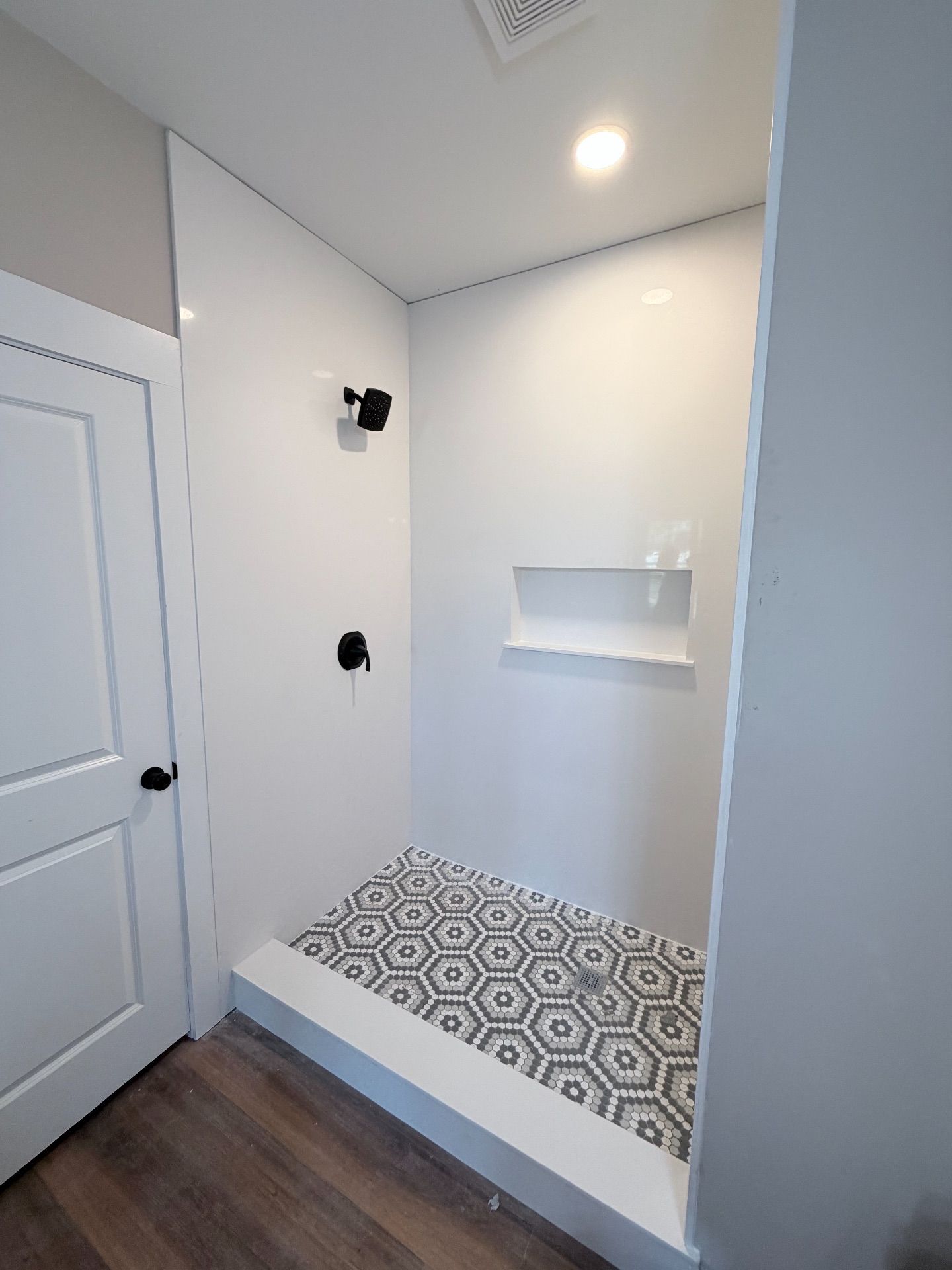 White bathroom with a tiled shower, black fixtures, and a recessed shelf.