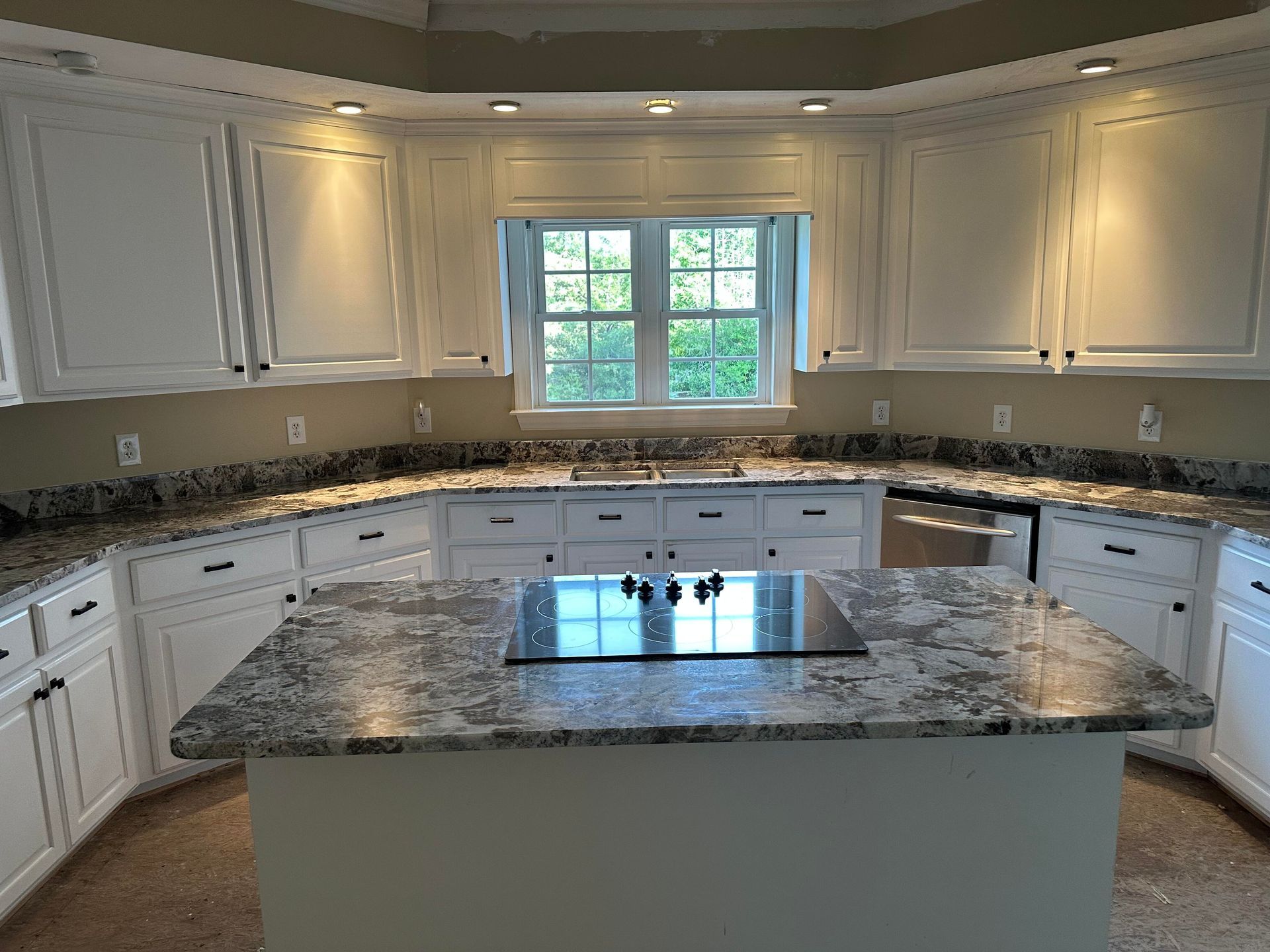 White kitchen with granite countertops, island with cooktop, and window.