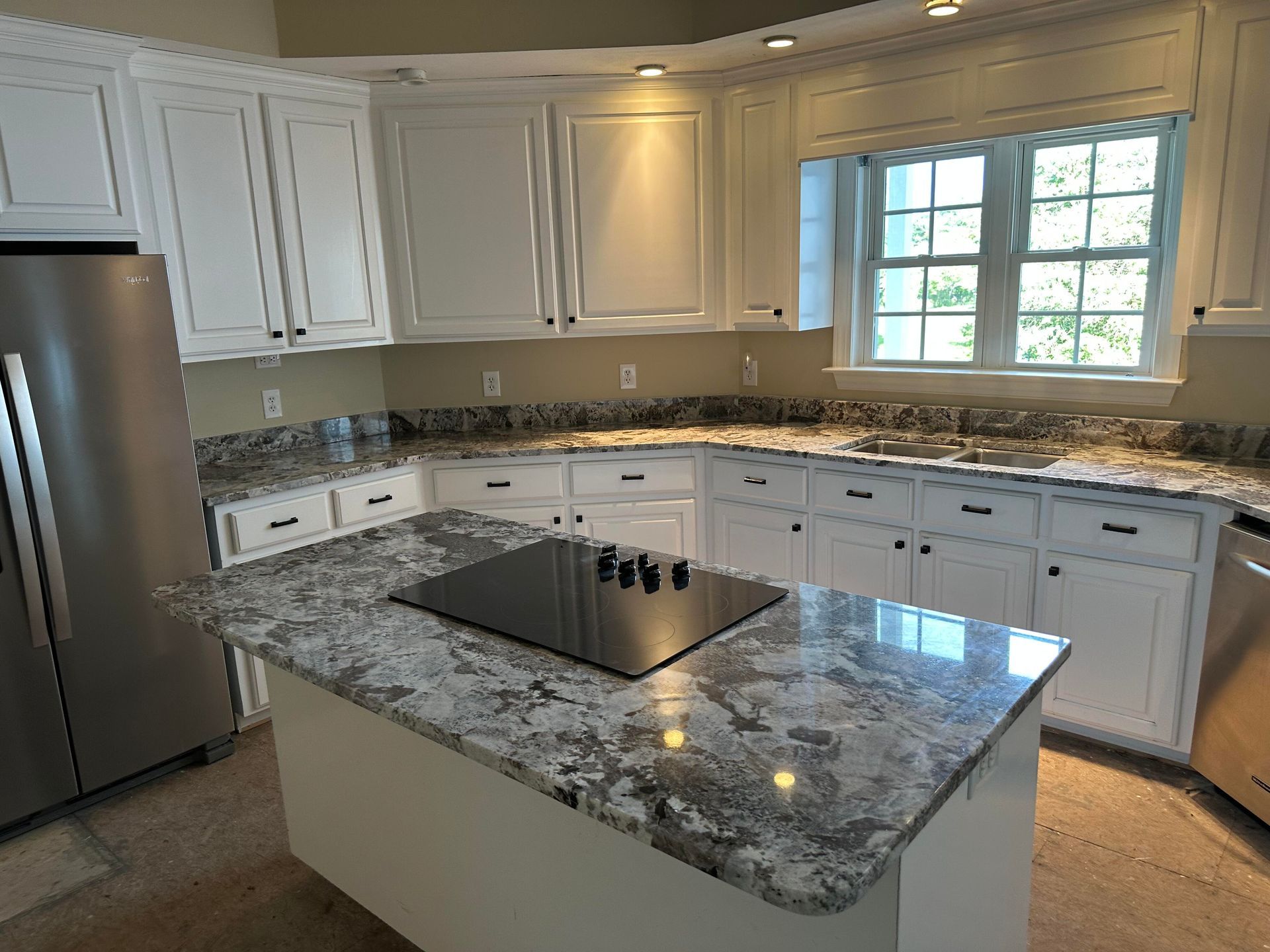 White kitchen with granite countertops, stainless steel appliances, and island with stovetop.