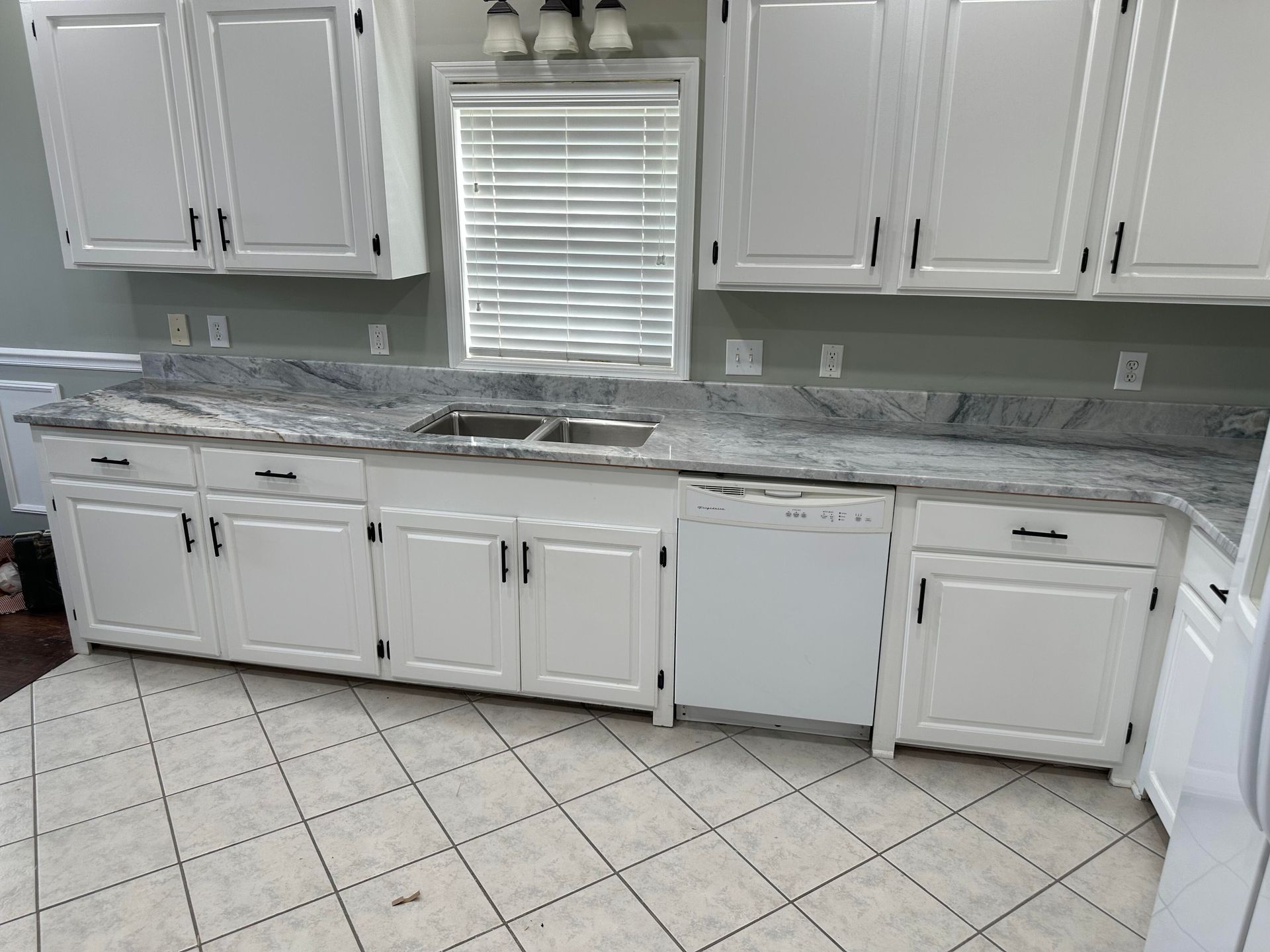 White kitchen cabinets with black hardware, granite countertops, and a white dishwasher.
