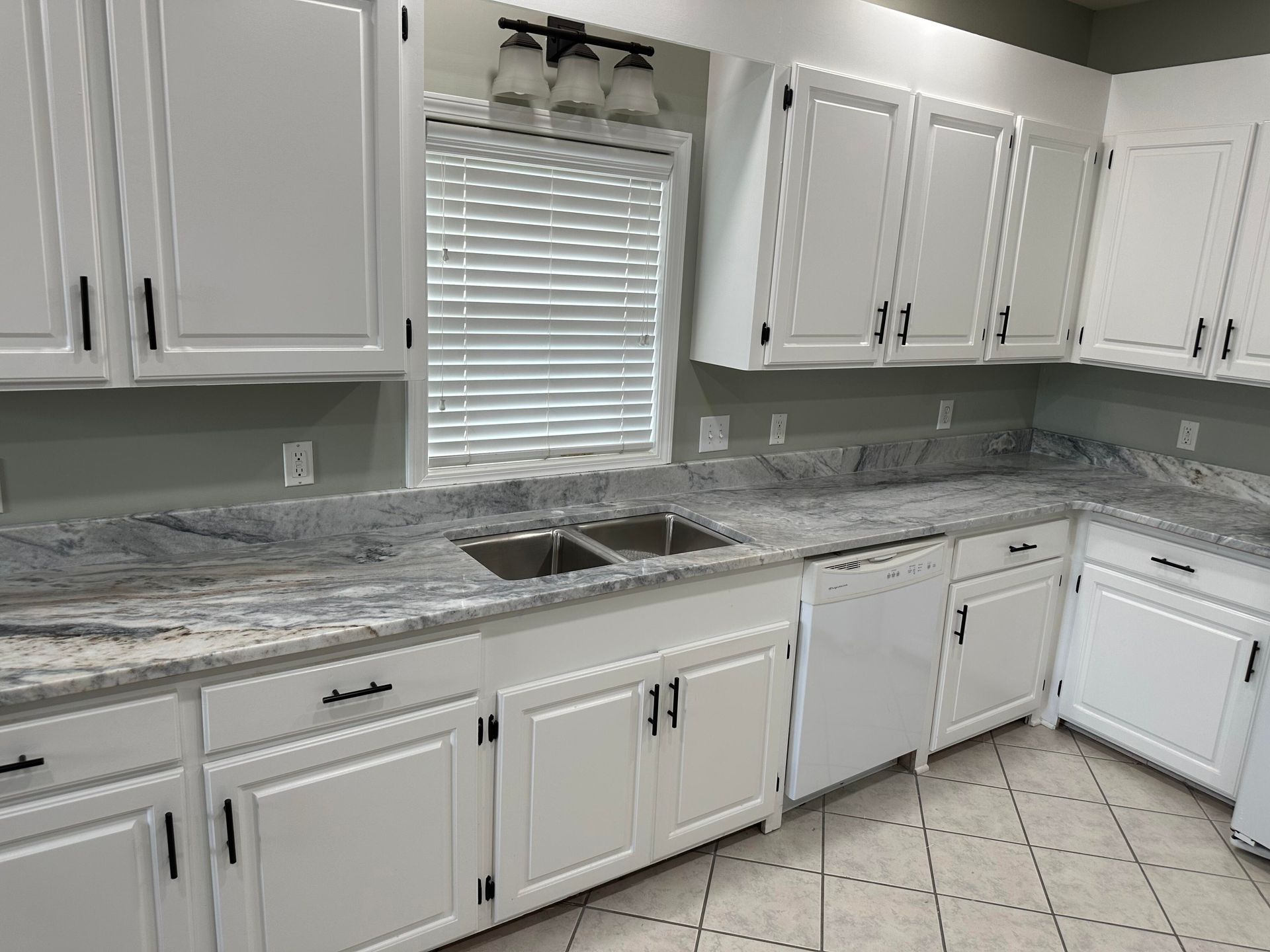 White kitchen cabinets with black handles, a white dishwasher, and gray countertops.
