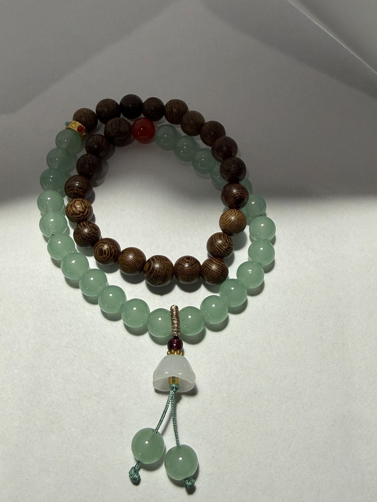 Dos pulseras de cuentas: una marrón y otra verde. La verde lleva un colgante.