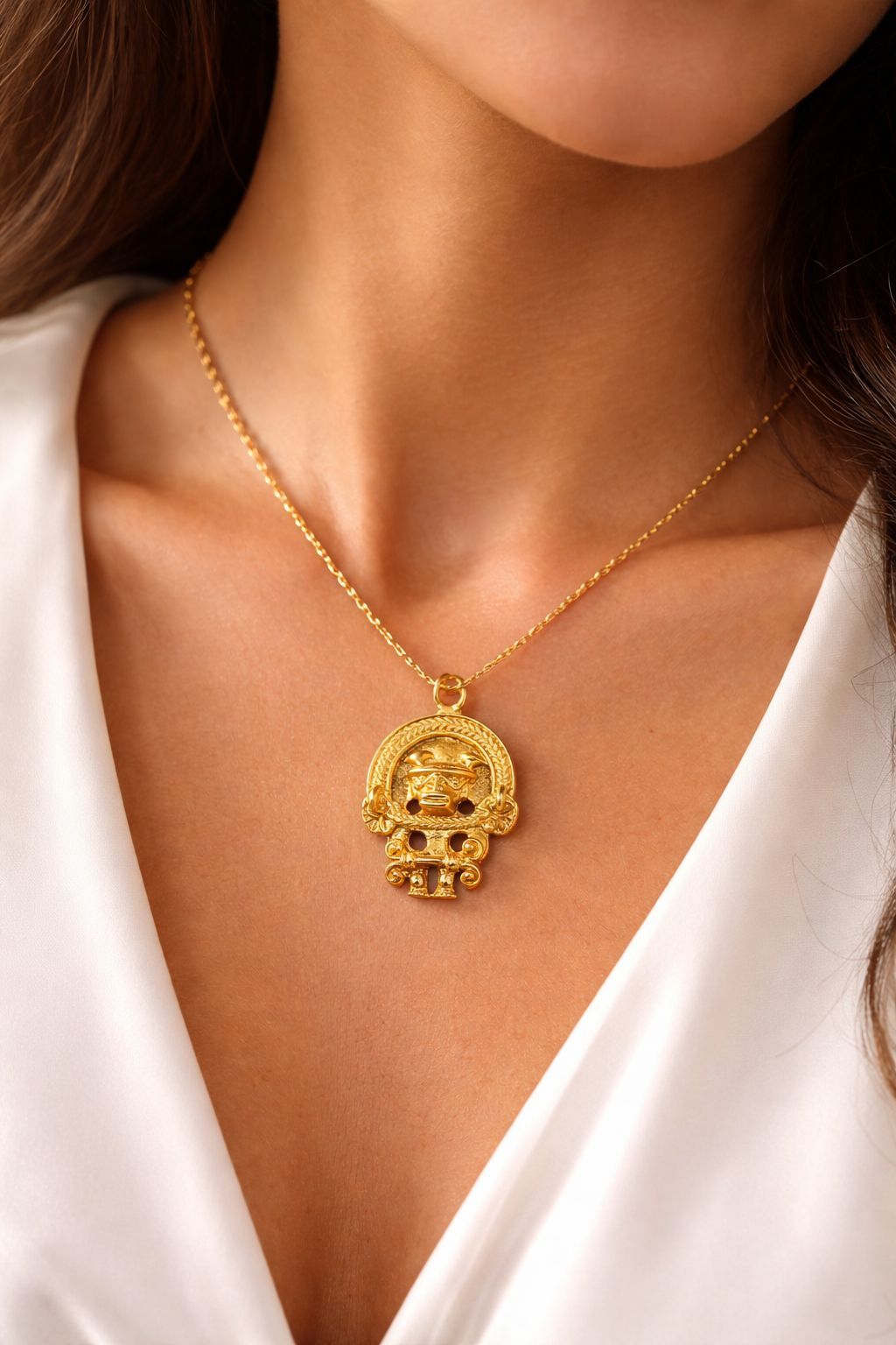 Un collar de oro con un colgante de medallón circular detallado, que se lleva sobre una blusa blanca.