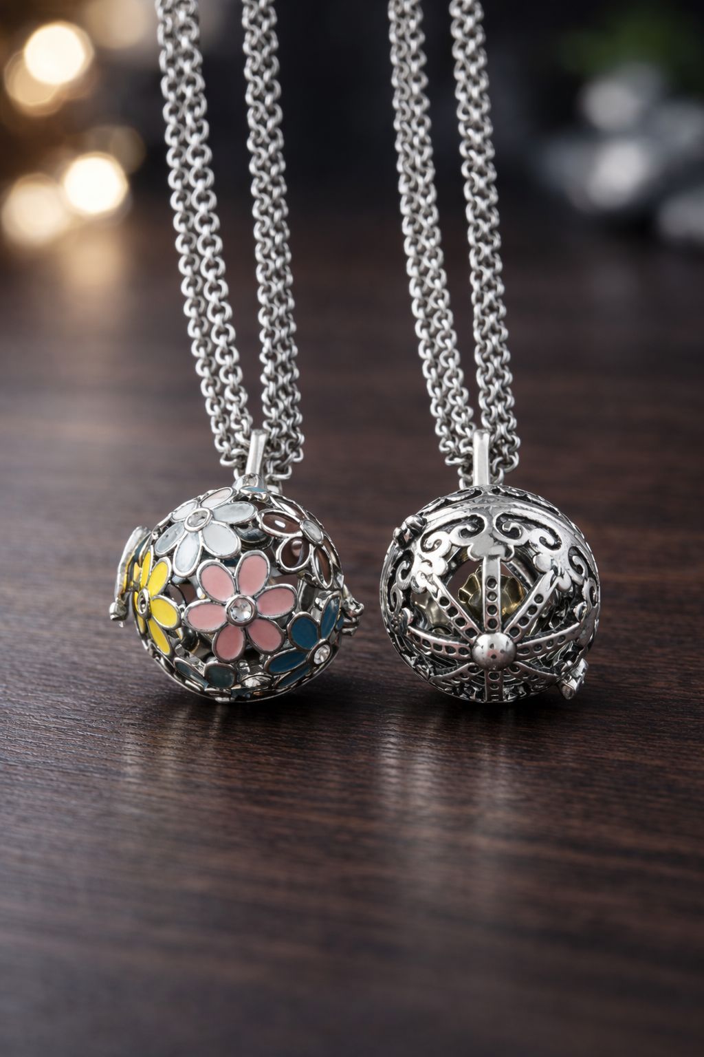 Dos colgantes esféricos de plata con forma de jaula, unidos por cadenas: uno con coloridos detalles florales esmaltados y el otro con intrincada filigrana.