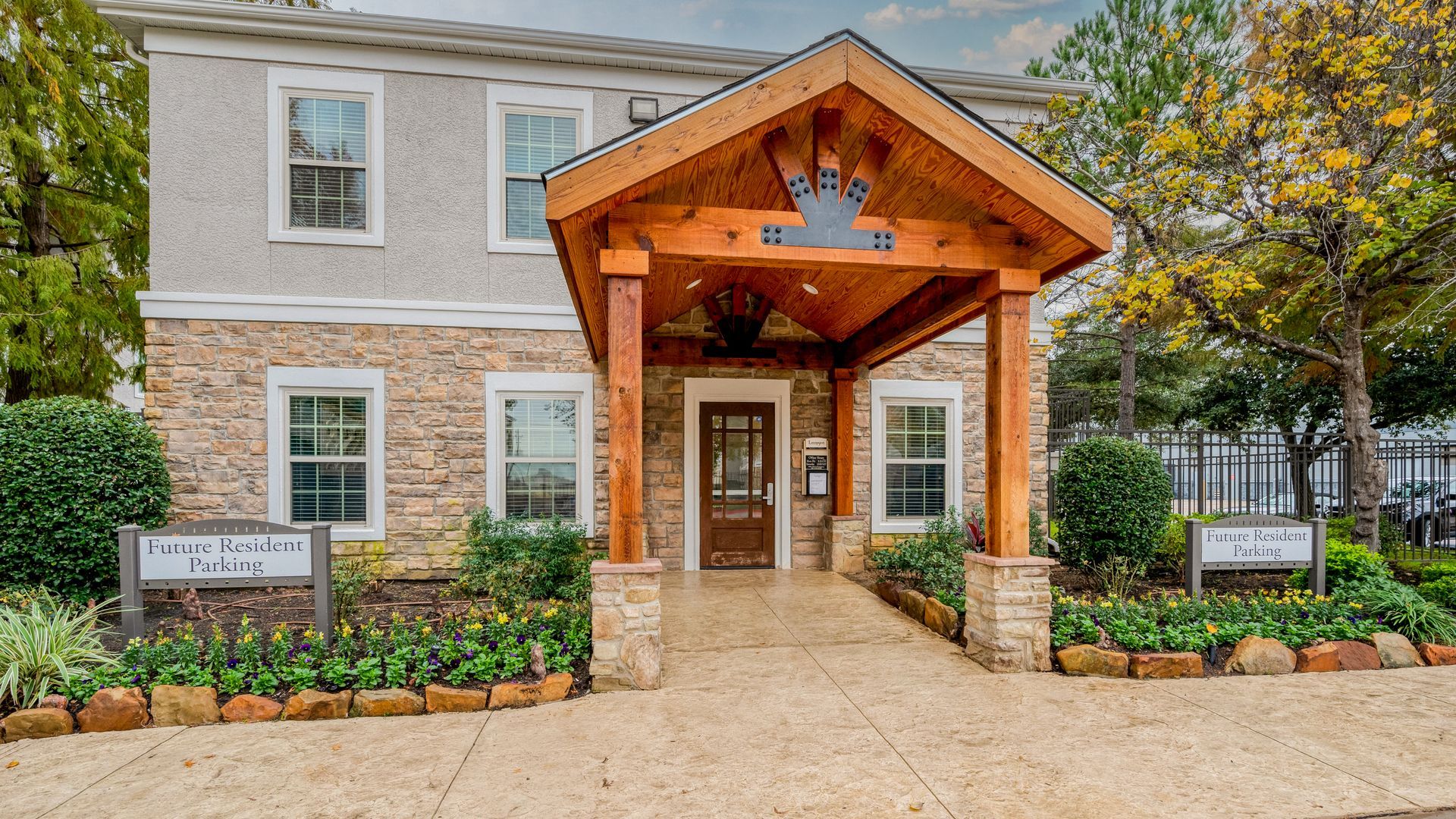 Entrance to building with wooden portico, stone facade, and landscaping.