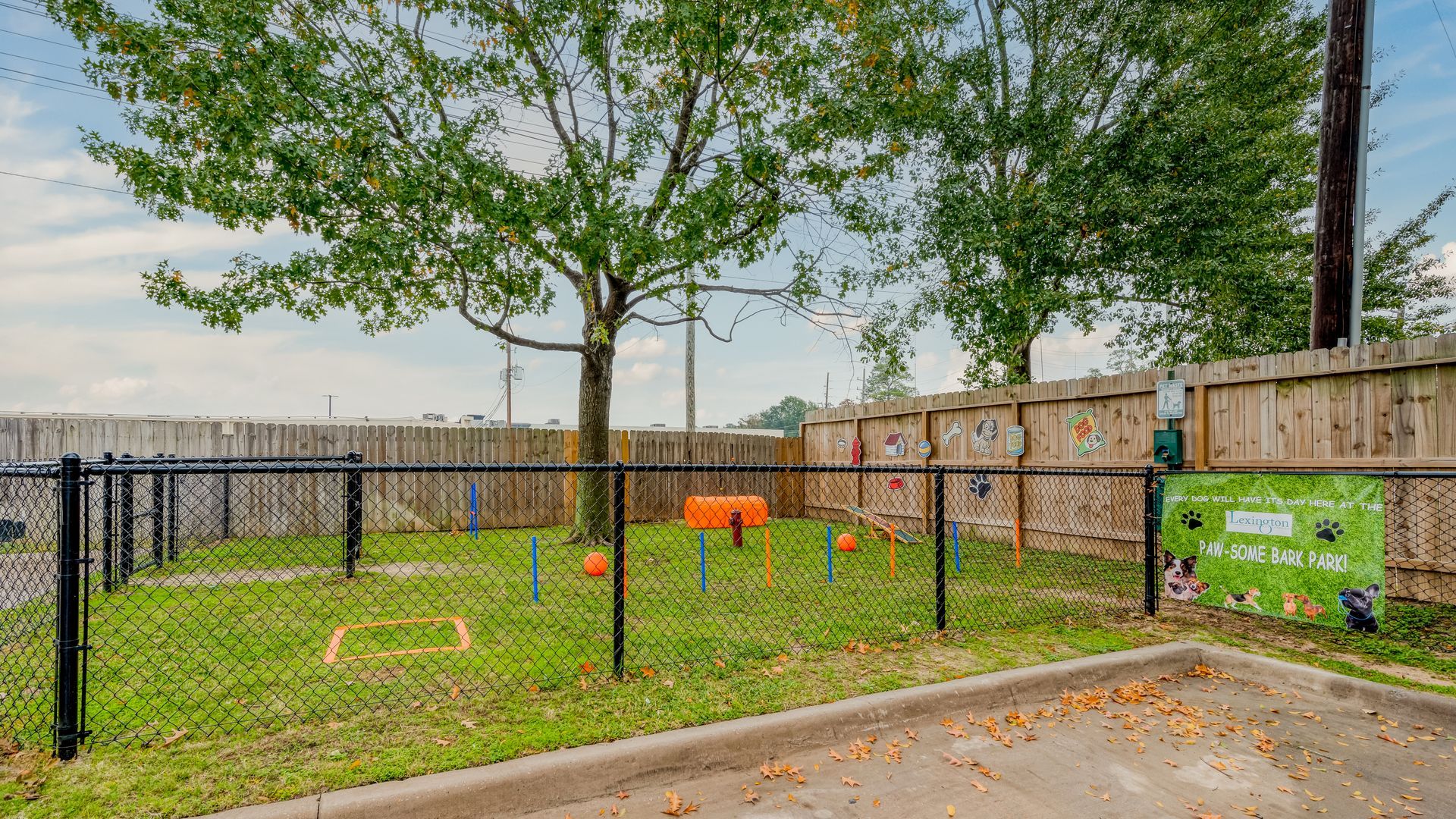 Dog park with agility equipment, fenced in, with trees and grass.