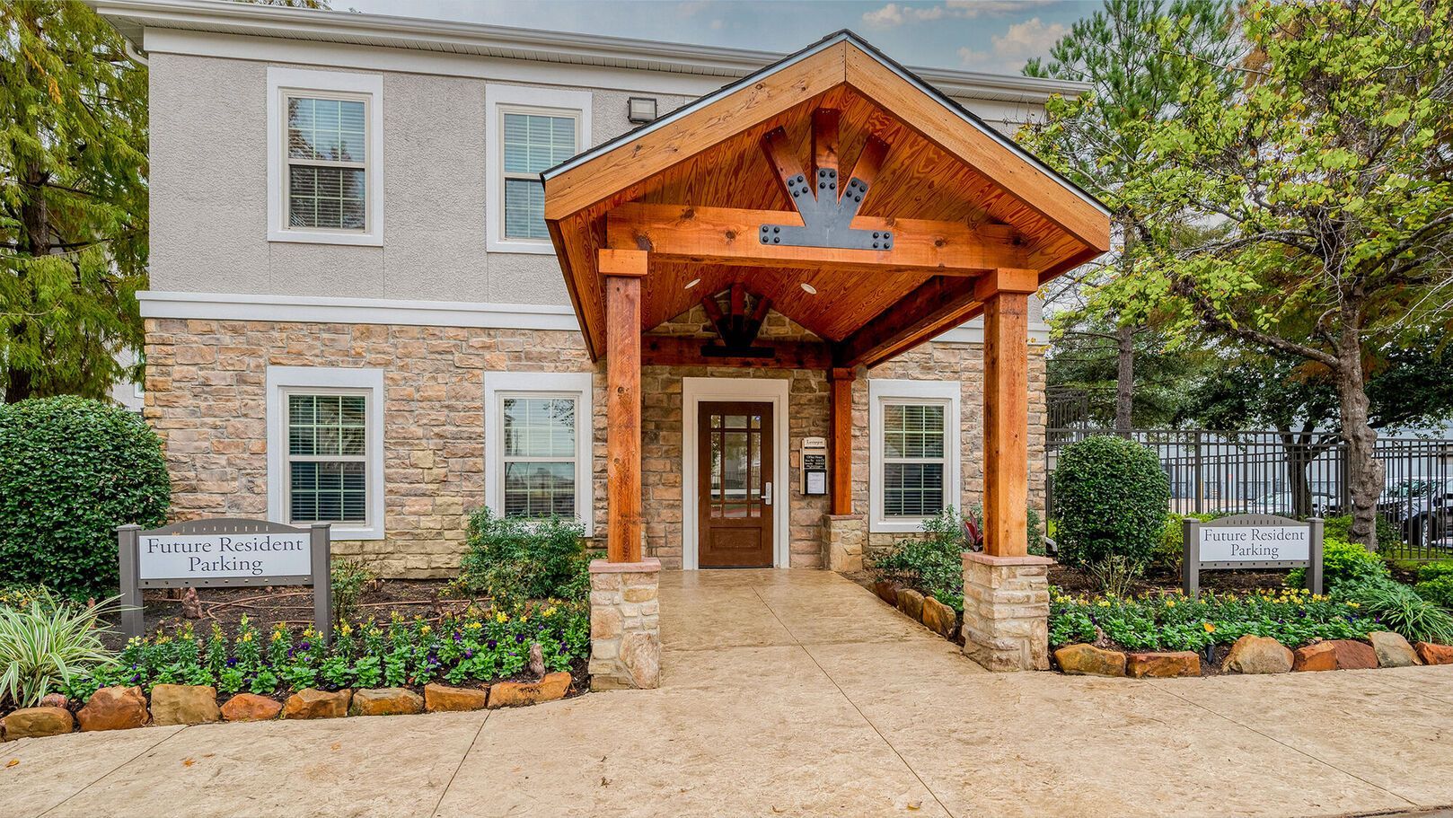A two-story building with stone siding and a prominent wooden portico entrance, framed by trees and manicured landscaping at Lexington at Champions in Houston, TX..