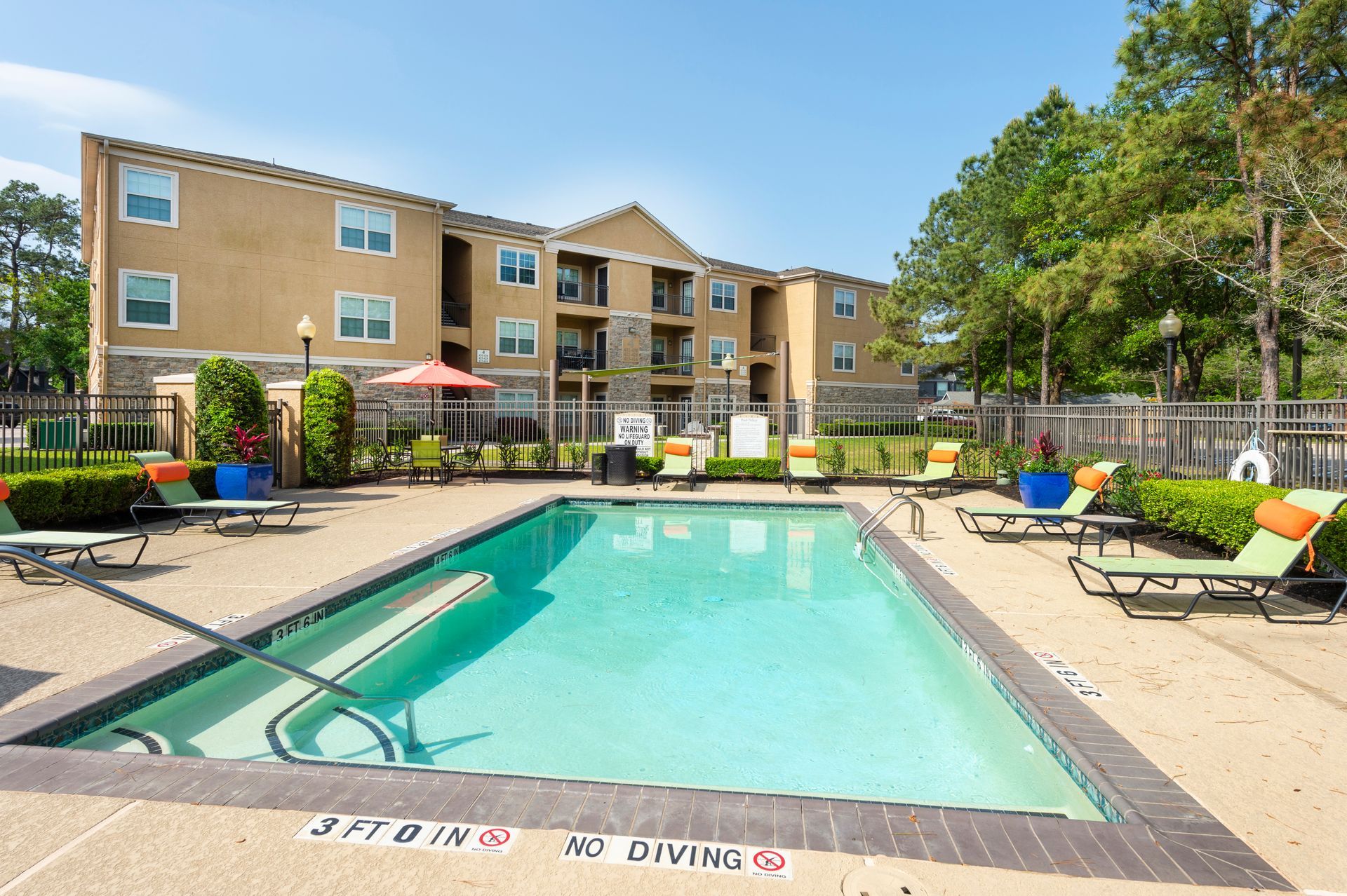 Outdoor swimming pool with lounge chairs and a multi-story apartment building in the background under a blue sky at Lexington at Champions in Houston, TX..