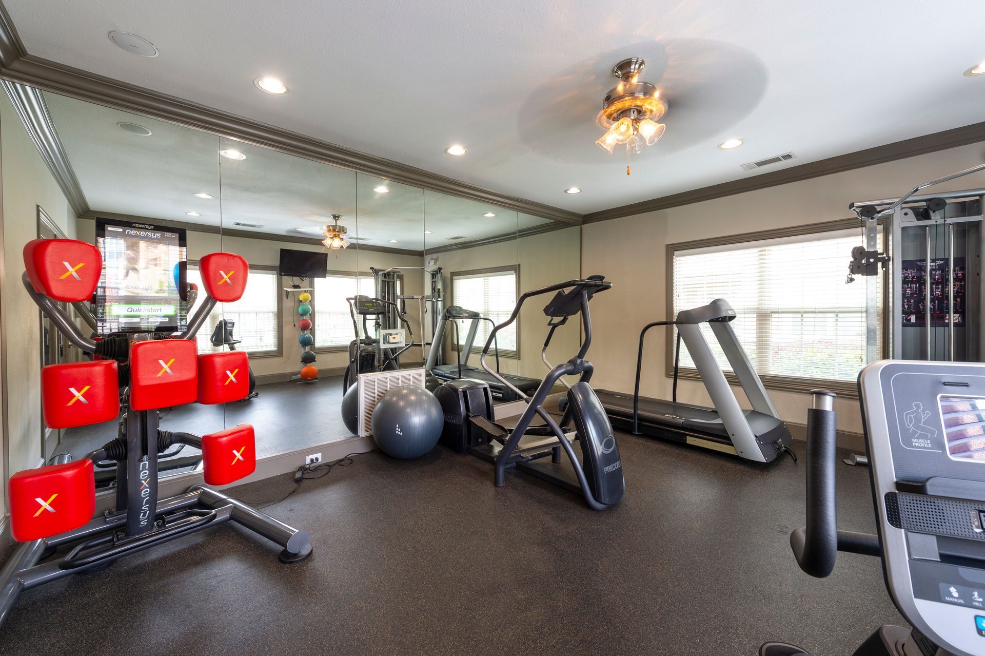 A gym interior featuring a red punch-bag station, a grey exercise ball, a cross-trainer, and a treadmill at Lexington at Champions in Houston, TX..