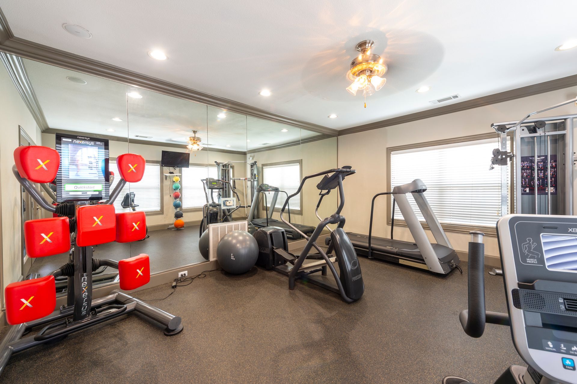 A small, indoor gym featuring a red striking target machine, a stationary bike, an elliptical, and a treadmill at Lexington at Champions in Houston, TX..
