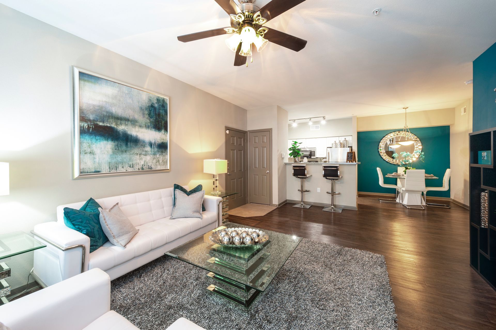 Modern living room with a white sofa, glass coffee table, and area rug, leading to a dining area with blue accent walls at Lexington at Champions in Houston, TX..