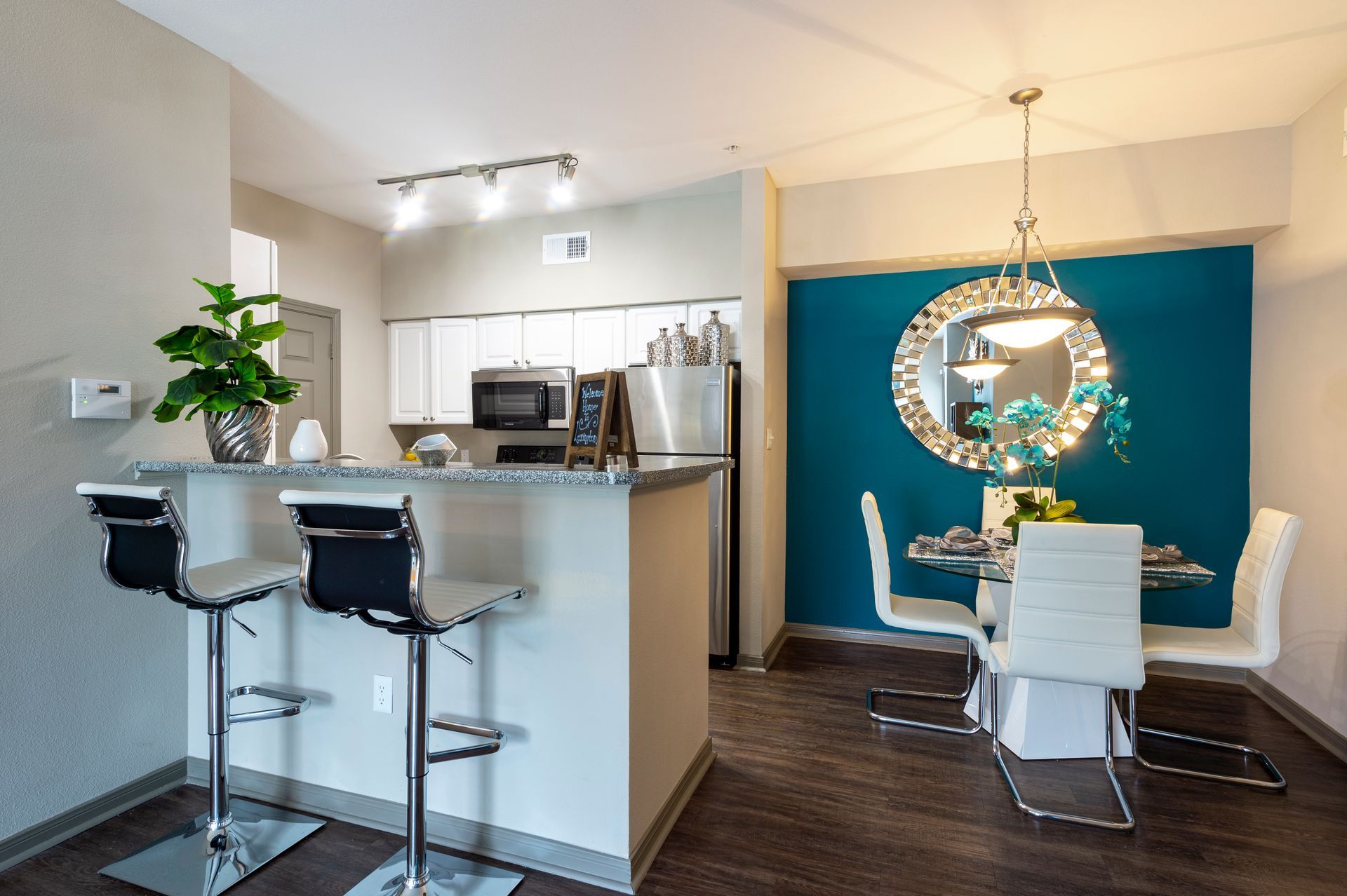 Modern kitchen featuring a breakfast bar with two black stools, open-plan dining area with teal wall and mirrored decor at Lexington at Champions in Houston, TX..