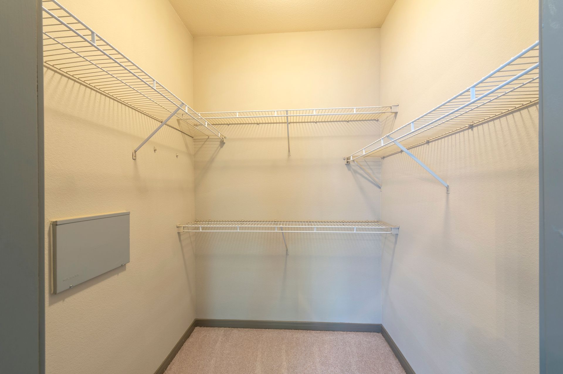 Empty walk-in closet with beige walls, light-colored carpet, wire shelving, and a small electrical panel on the wall at Lexington at Champions in Houston, TX.